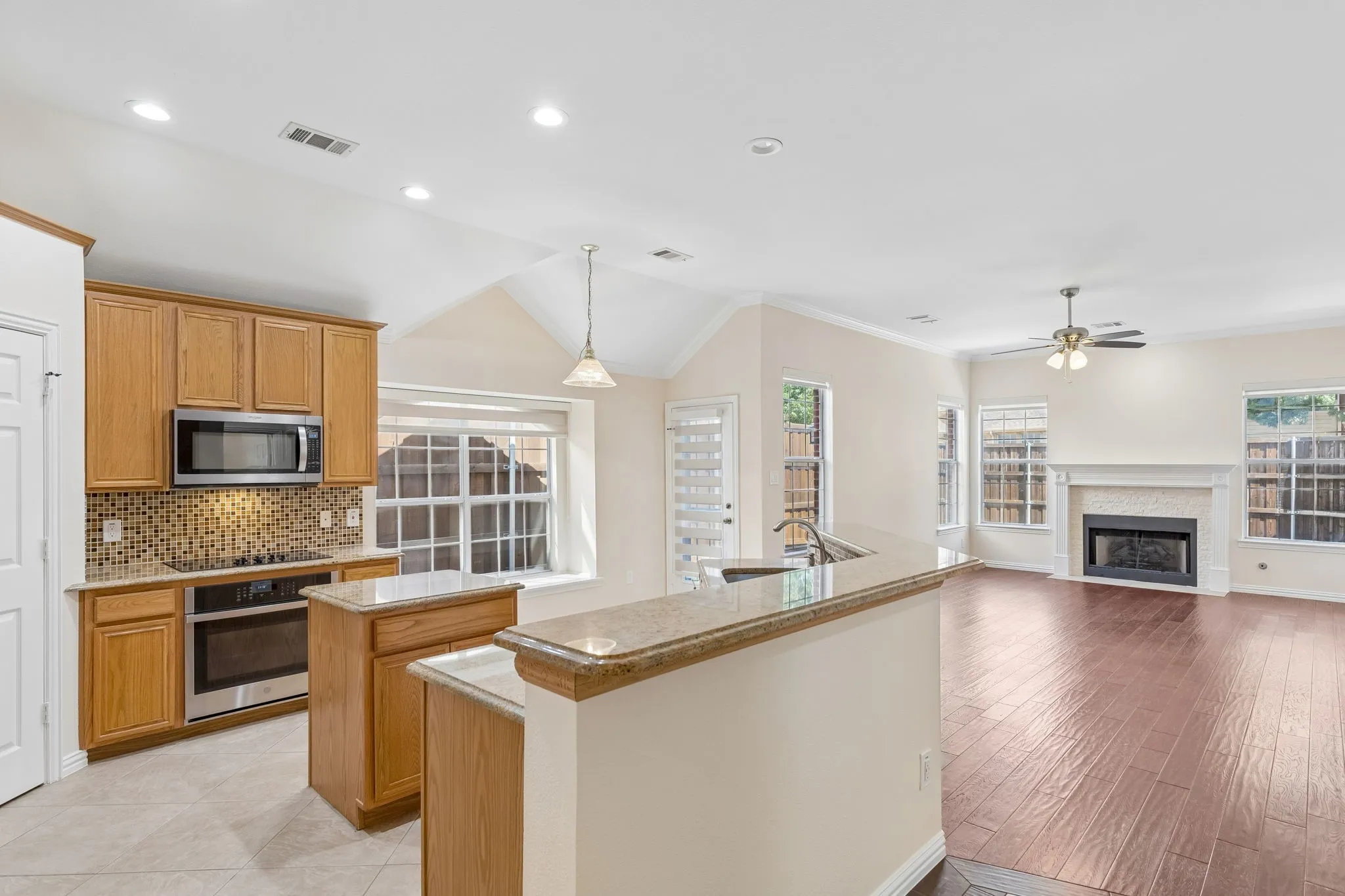 Open concept living area featuring a kitchen with wood cabinetry, stainless steel appliances, and a mosaic tile backsplash