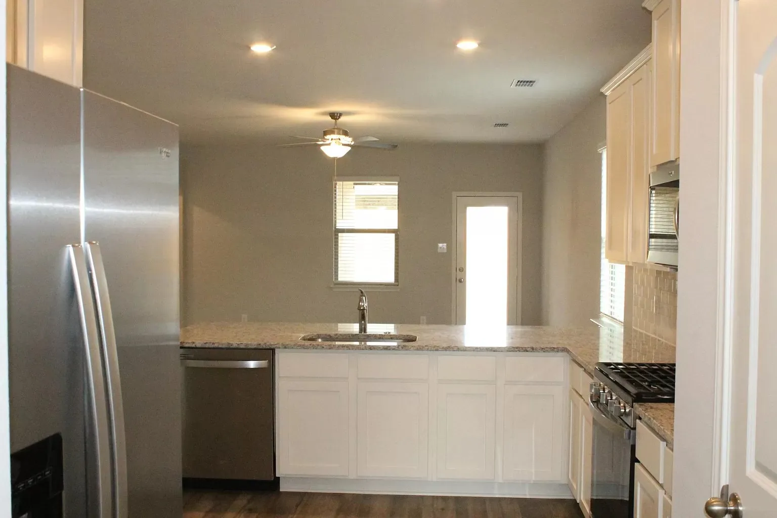 Kitchen featuring stainless steel appliances, white cabinetry, speckled countertops, a tile backsplash, and wood-finish flooring