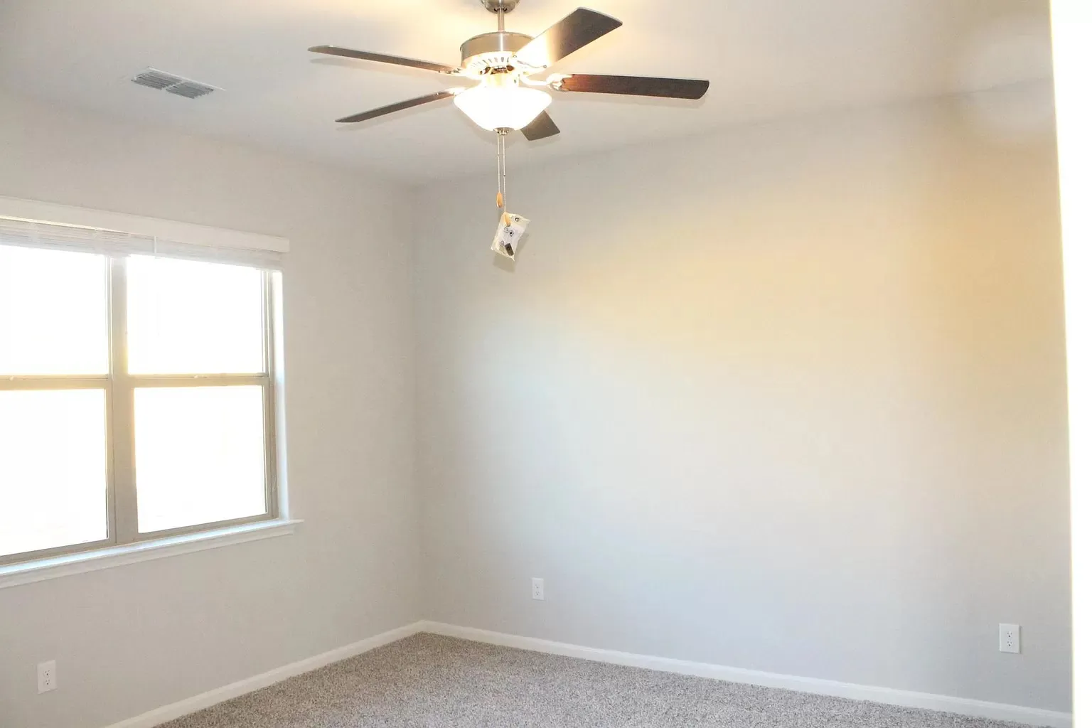 Expansive window with roller shade, ceiling fan with integrated lighting, and carpeted flooring