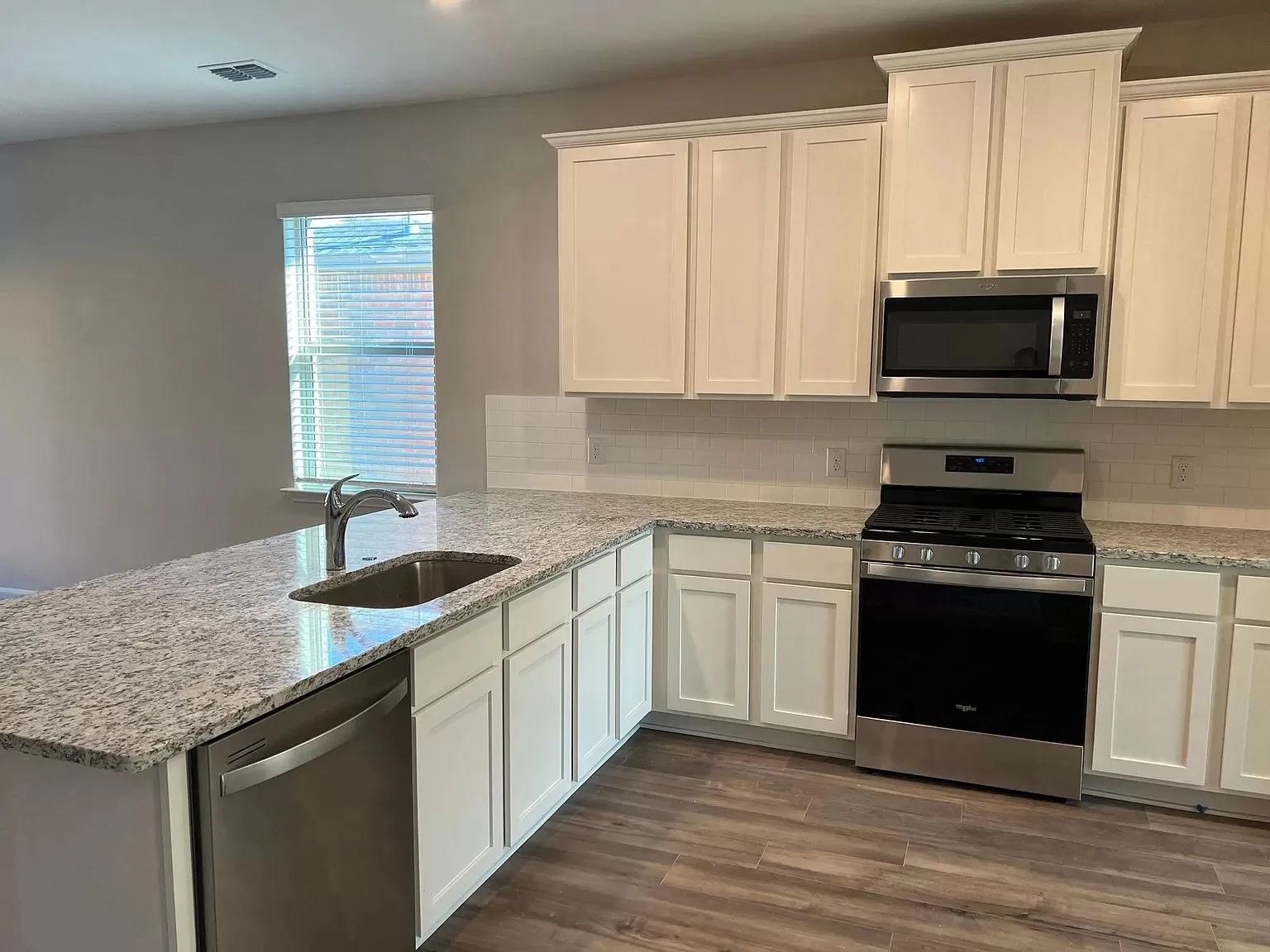 White shaker-style cabinetry, granite countertops, subway tile backsplash, stainless steel appliances, and wood-finish flooring