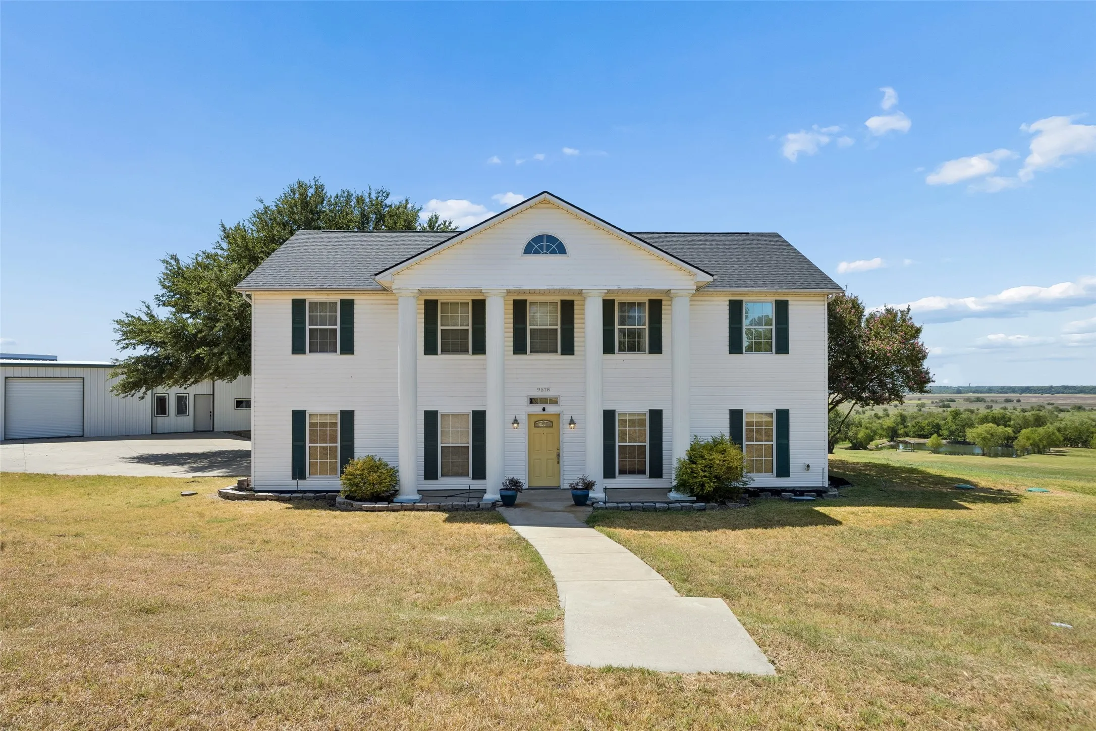 Two-story colonial exterior with prominent columns, dark shutters, and a yellow entry door