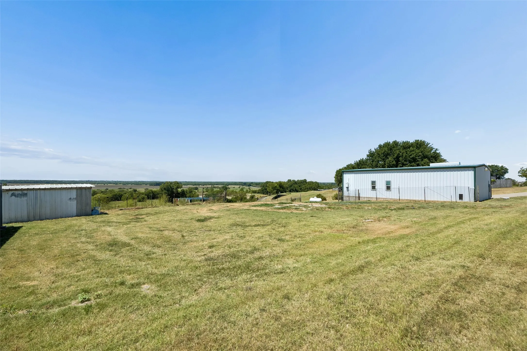 Expansive open field featuring two detached structures and a distant tree line