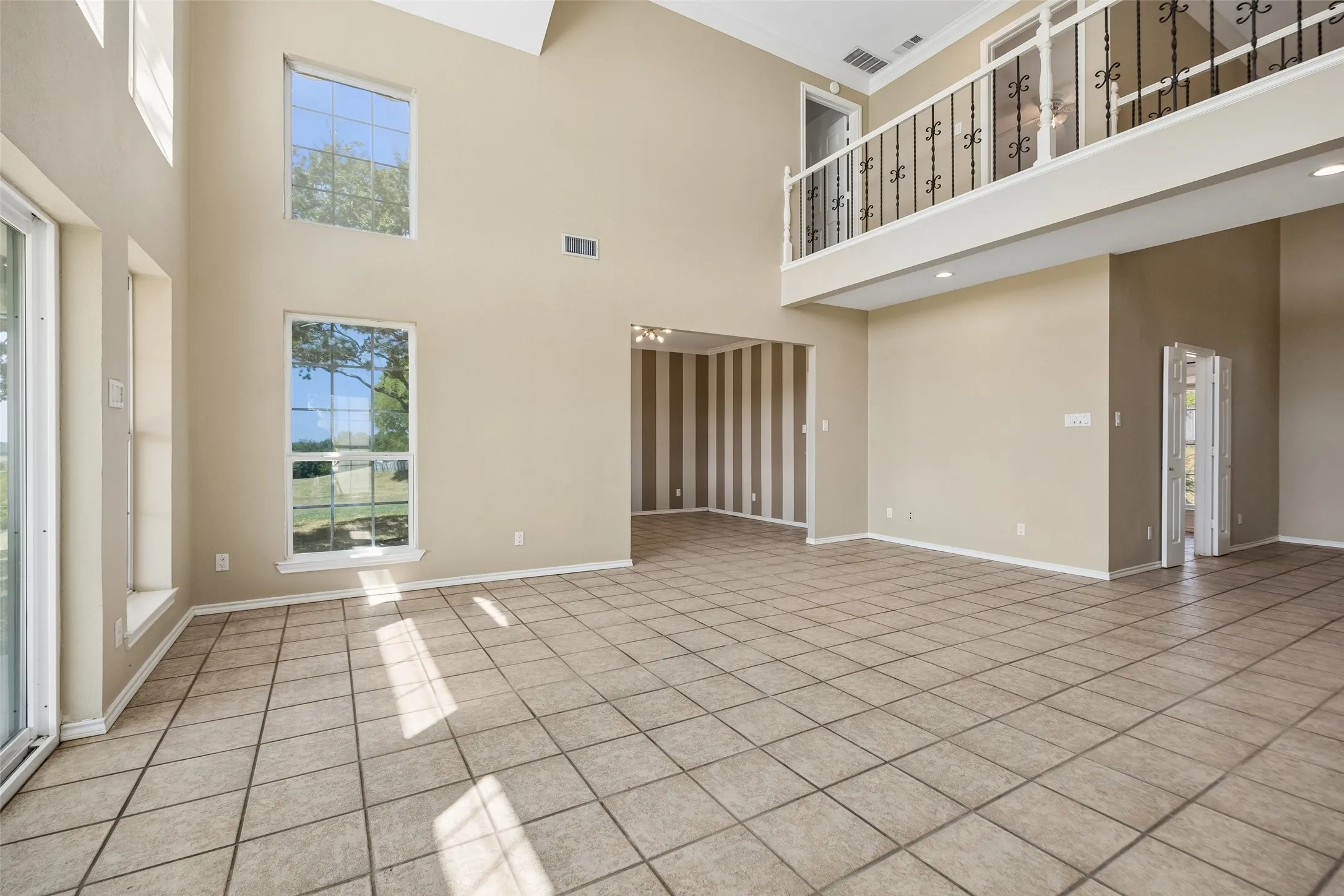 Expansive open-concept living area featuring tile flooring, a white mantel fireplace, and a second-story overlook with decorative wrought iron railing