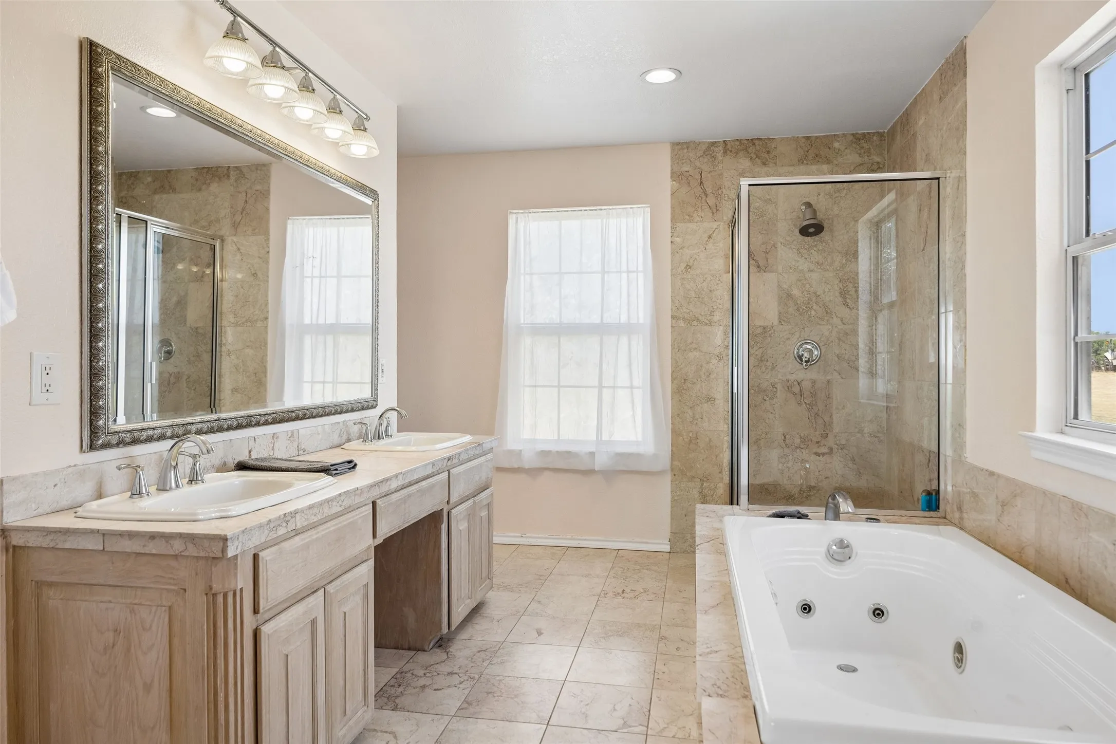 Second floor Primary Bath Dual vanity with integrated sinks, a large framed mirror, a jetted soaking tub, a tiled walk-in shower with a glass enclosure, and tiled flooring