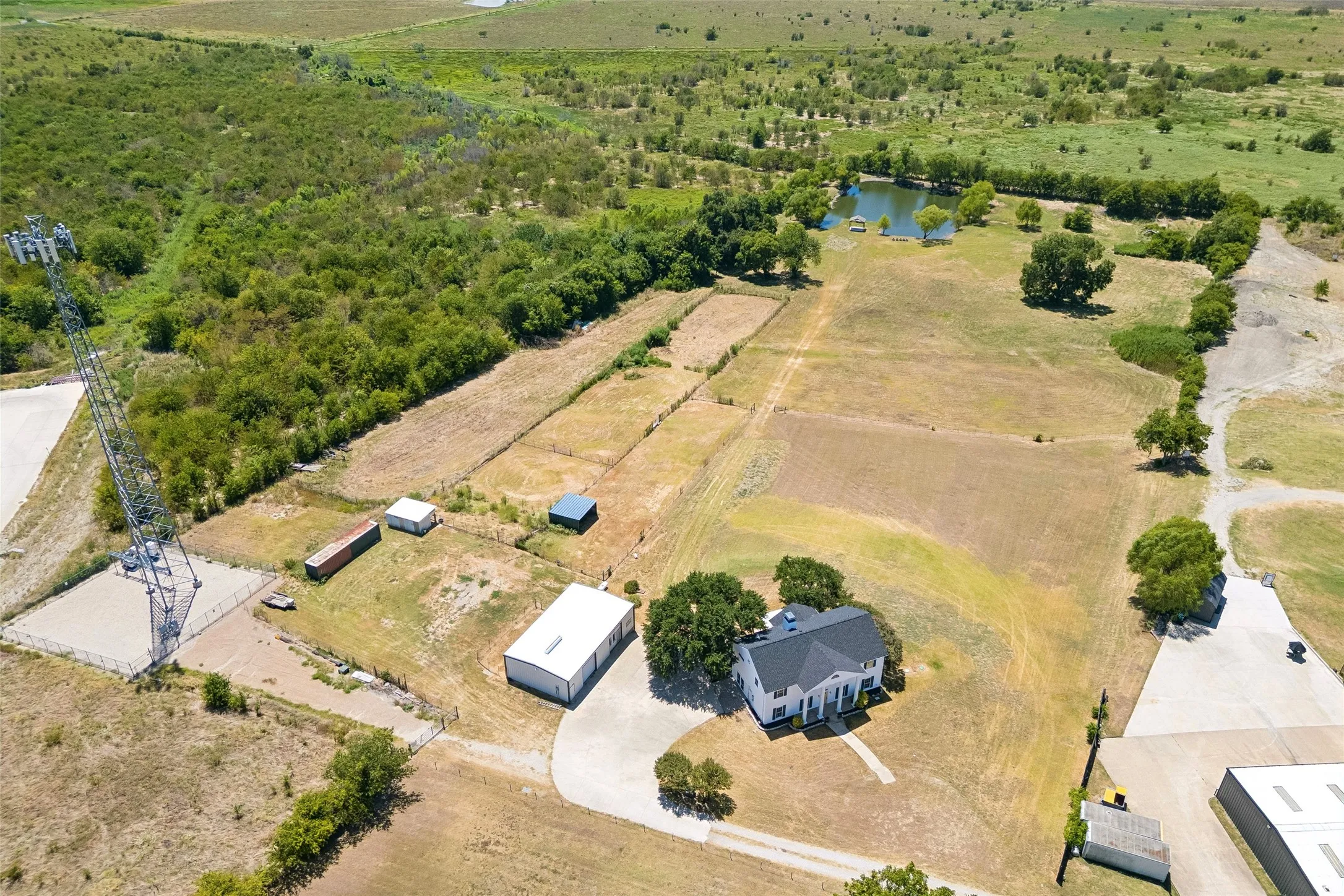 Expansive property featuring a two-story residence, separate outbuilding, gravel driveway, pond, and surrounding open land