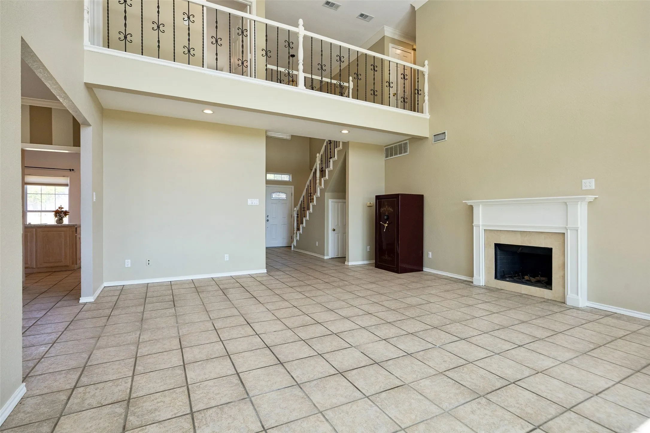 Expansive open-concept living area featuring tile flooring, a white mantel fireplace, and a second-story overlook with decorative wrought iron railing