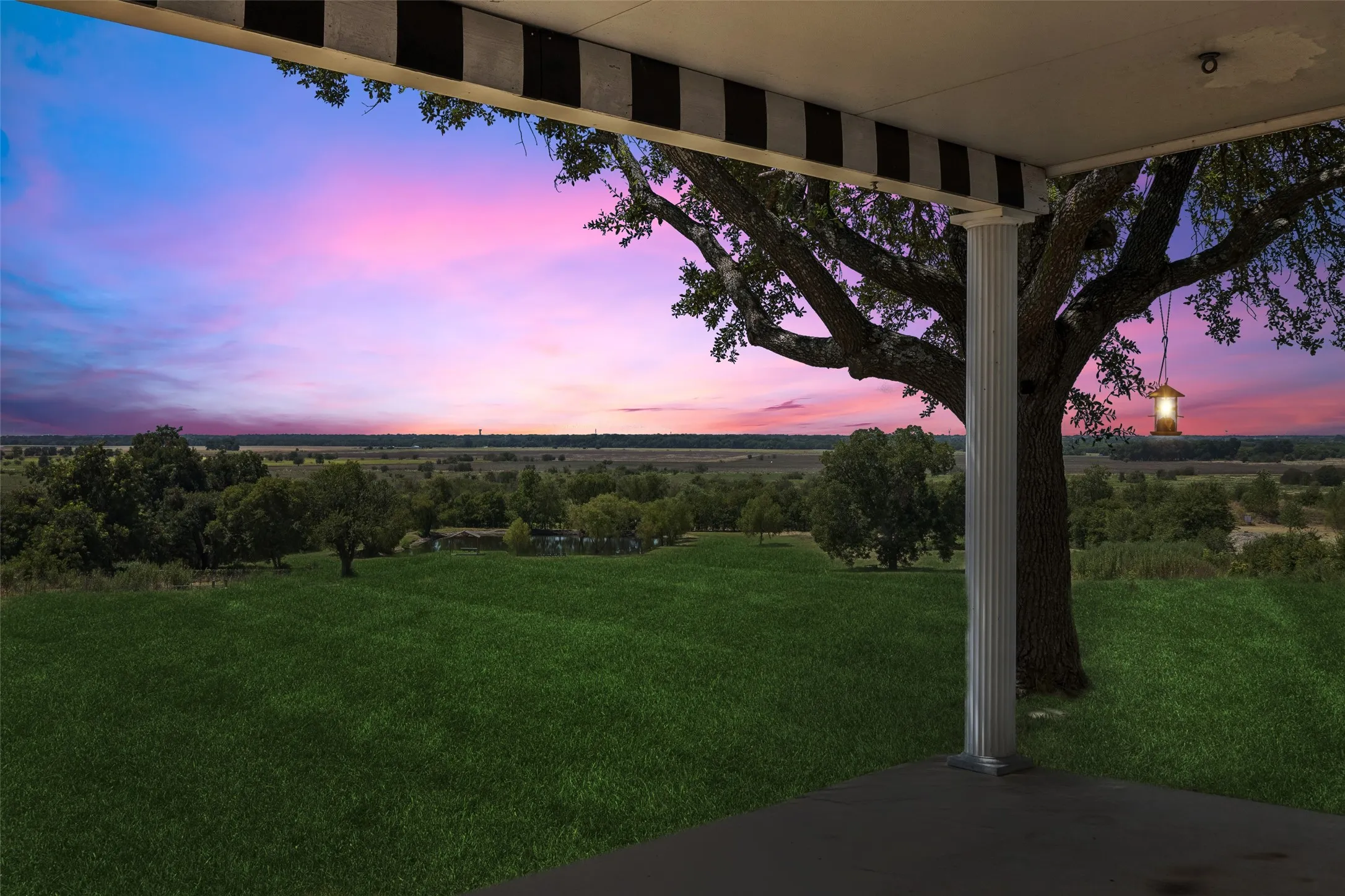Covered patio with a fluted column, overlooking an expansive grassy area and distant trees