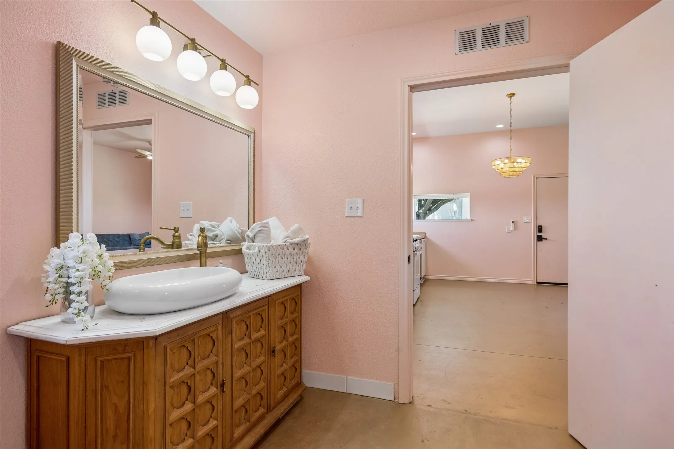 Full bathroom inside MIL or Guest Suite inside metal building adjacent to shop with brass shower fixture, white vessel sink, wood-finish vanity with carved details, and polished gold-tone wall-mounted light fixtures