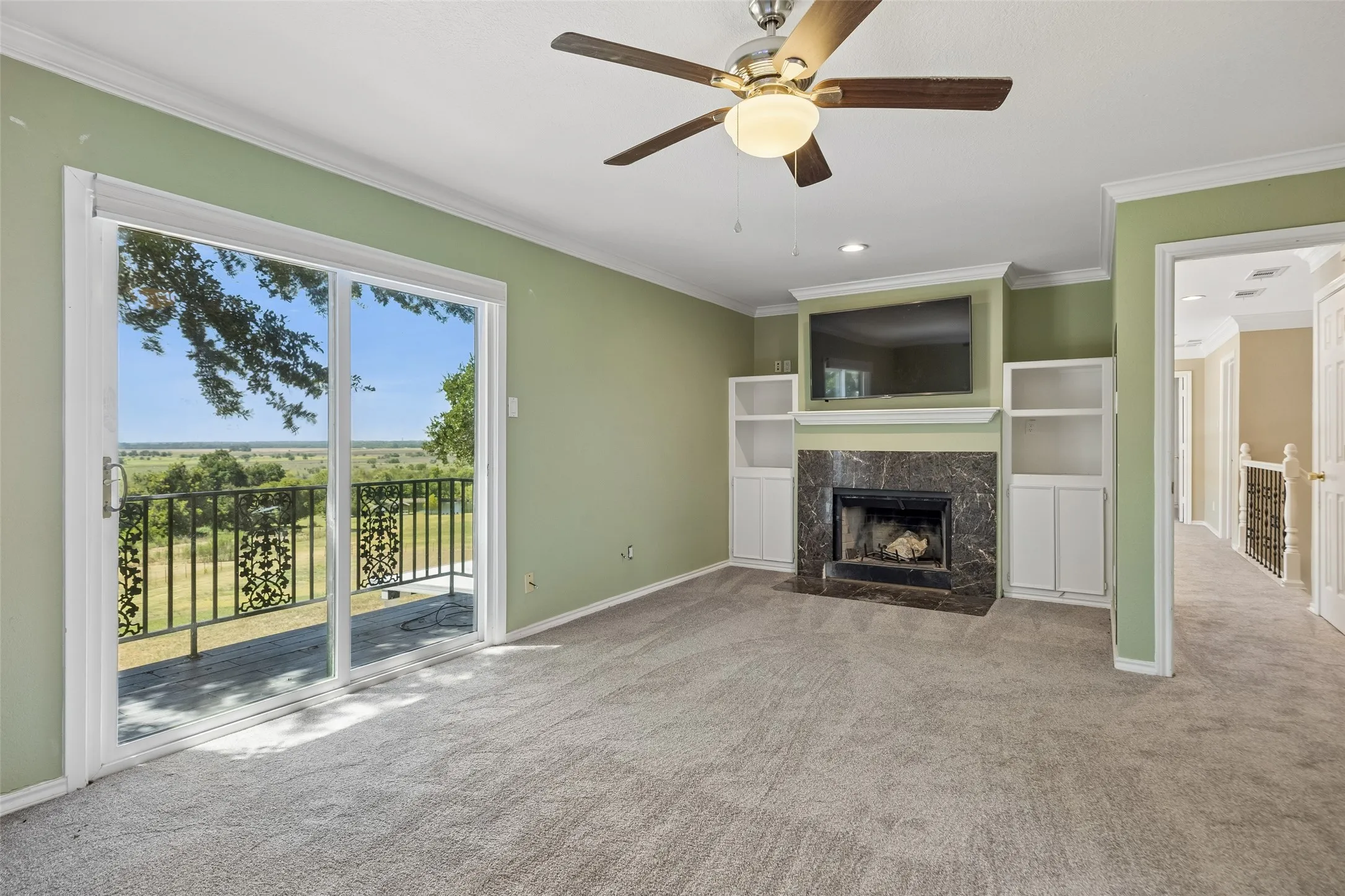 Second floor Primary bedroom Sliding glass door opening to a balcony with decorative railing, dark stone fireplace with mantel, built-in shelving, carpeted flooring, and a ceiling fan