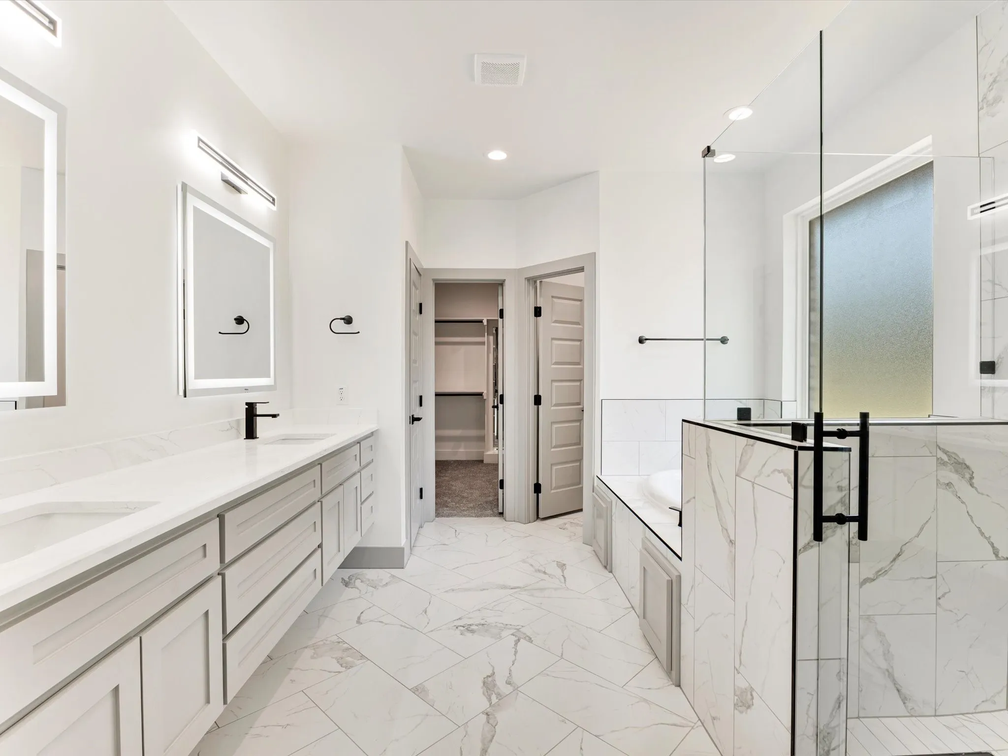 Dual vanity with integrated sinks, frameless glass shower enclosure, separate soaking tub, and walk-in closet with shelving