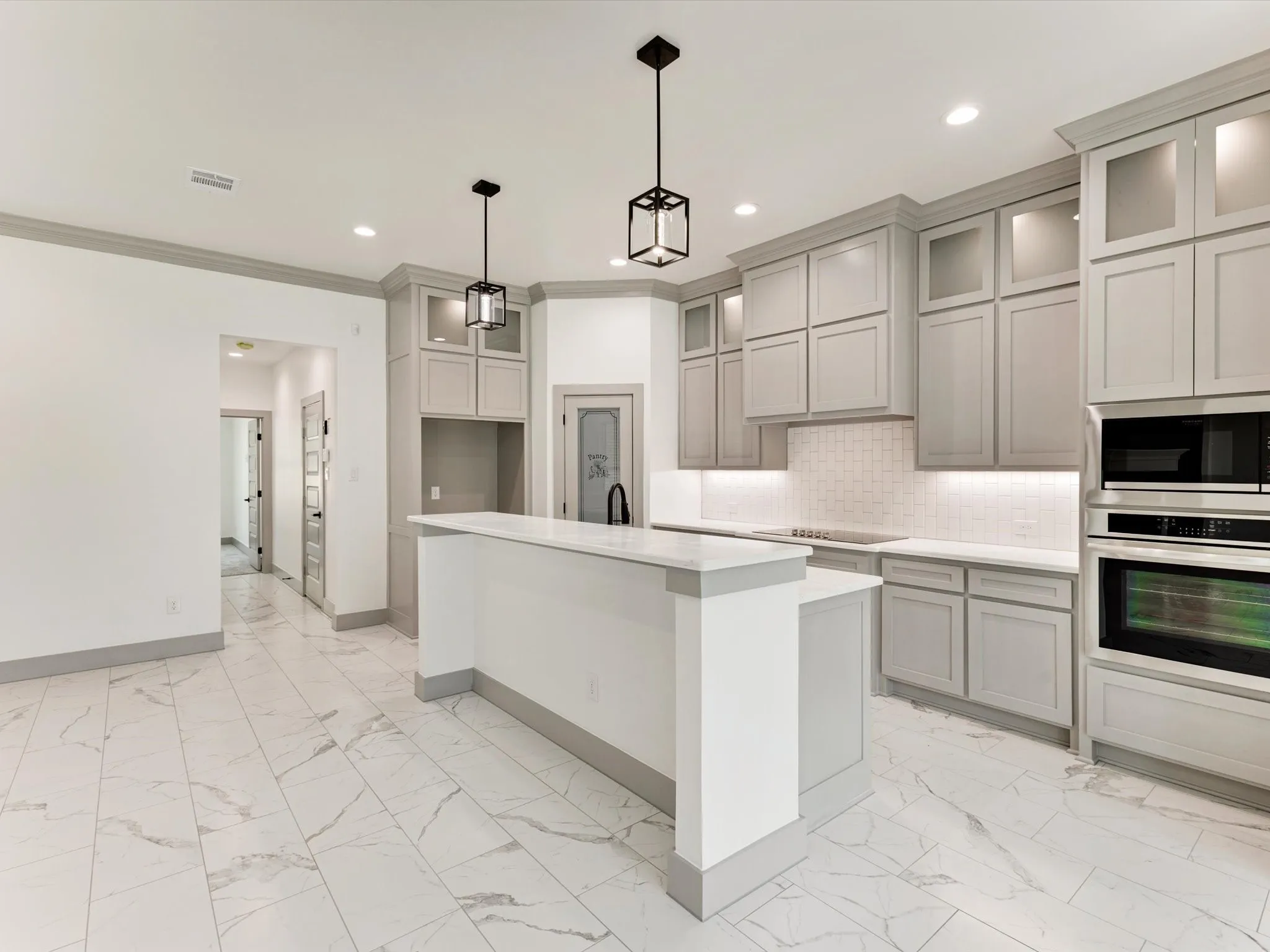 Open-concept kitchen featuring gray shaker-style cabinetry, a built-in oven and microwave, white quartz countertops, and marble-look tile flooring