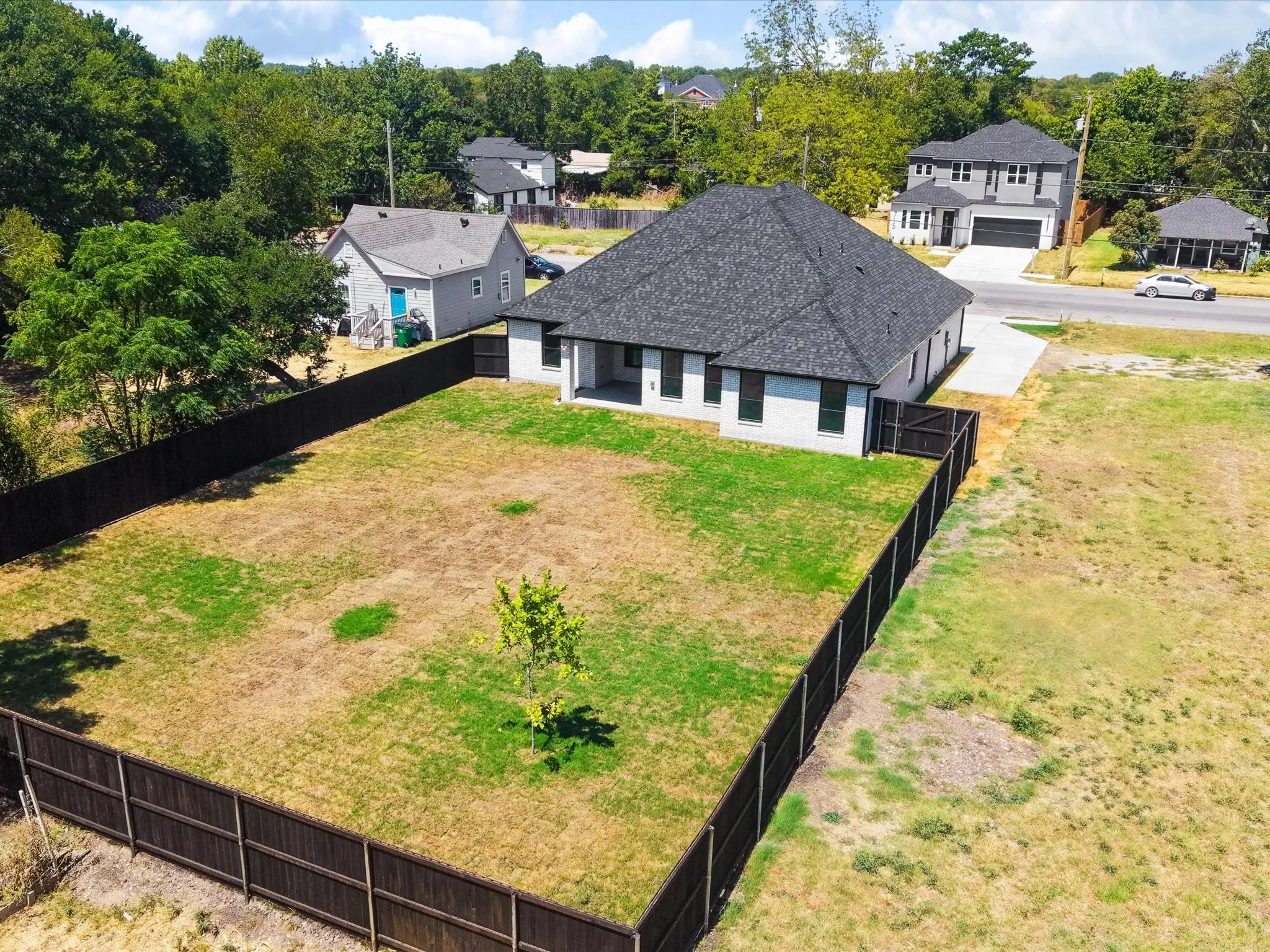 Newly constructed residence featuring a dark shingle roof, light-colored exterior siding, and a spacious enclosed backyard with a wood fence