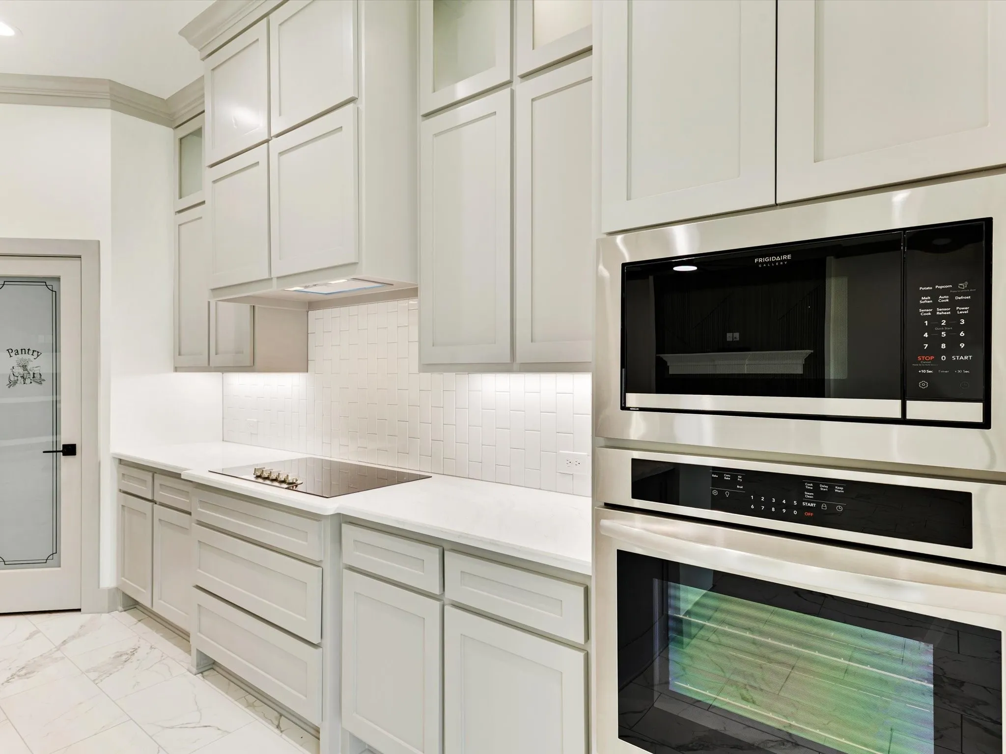 Built-in stainless steel appliances, induction cooktop, white shaker-style cabinetry, quartz countertops, and a full tile backsplash