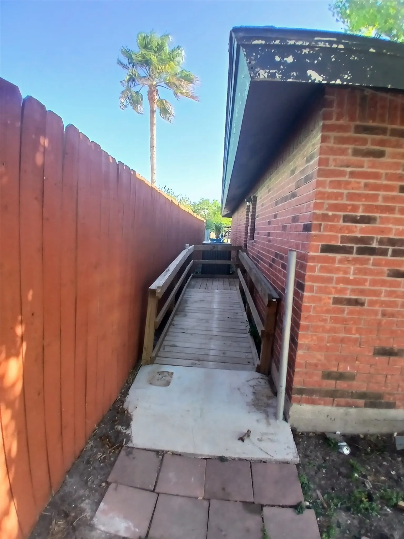 Brick exterior with a wooden privacy fence, leading to a wooden ramp with handrails