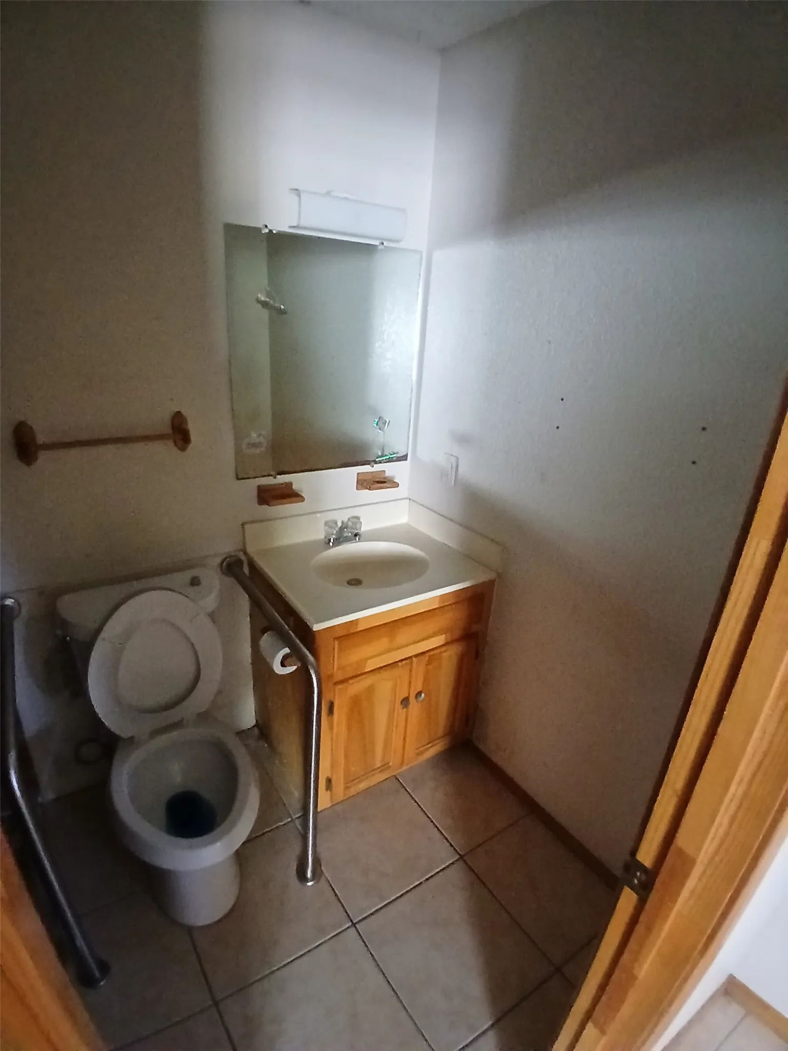 Vanity with a white countertop and natural wood-finish cabinetry, a wall-mounted mirror, and tile flooring