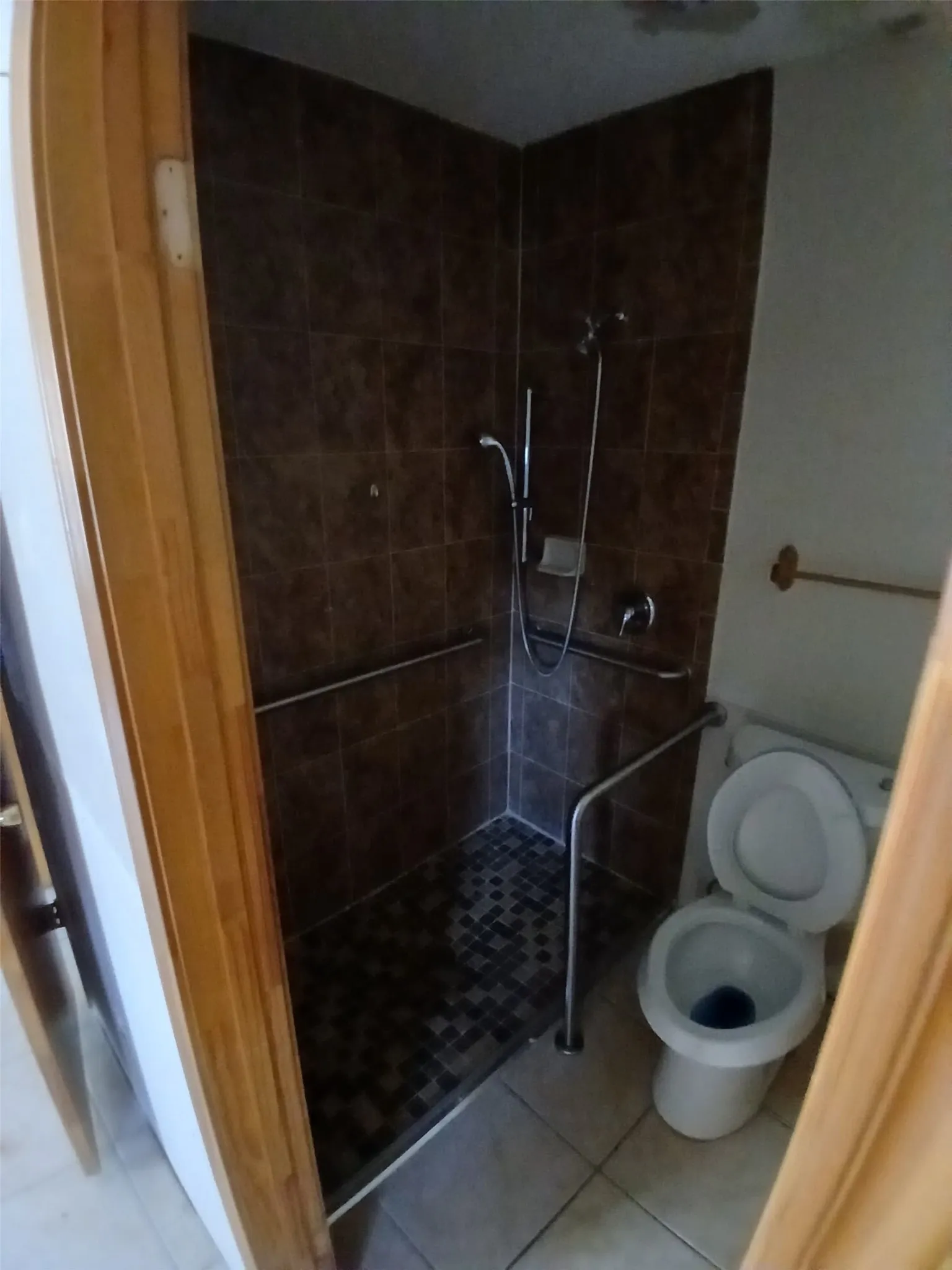 Tile-surround shower with a mosaic tile floor, integrated grab bars, and a wall-mounted showerhead
