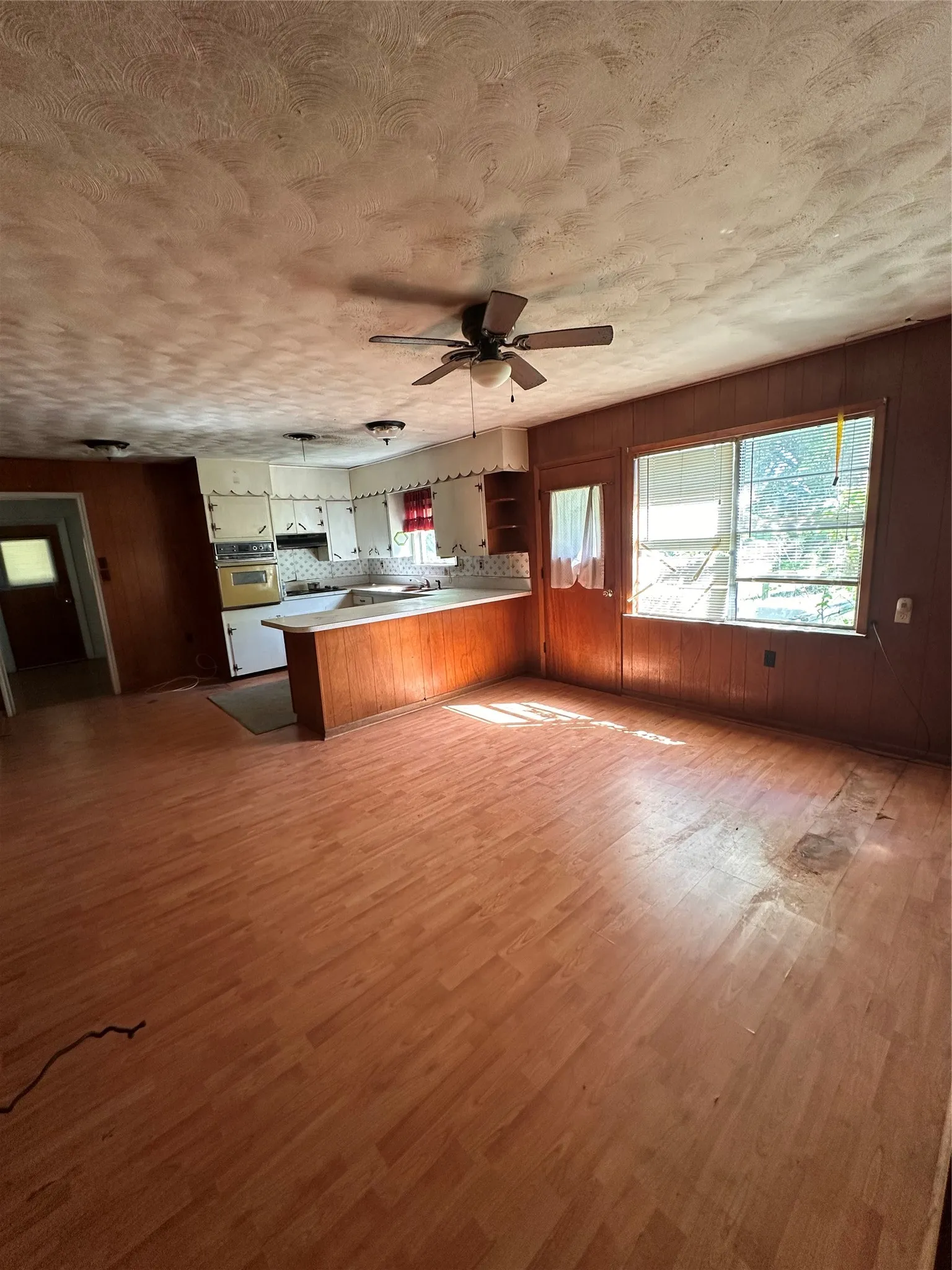 Wood-finish flooring, paneled walls, ceiling fan with integrated lighting, built-in kitchen cabinetry, and multiple windows