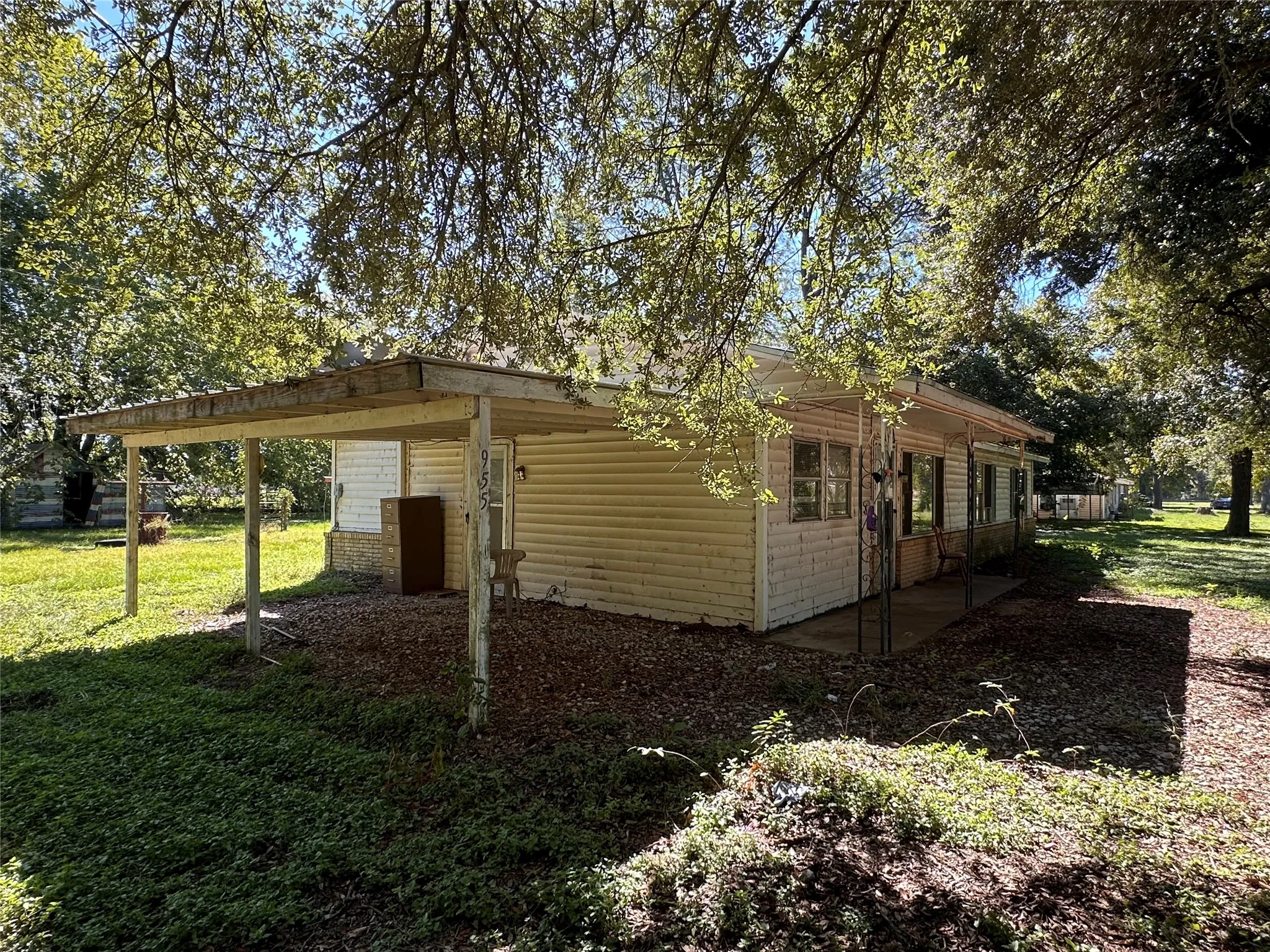 Exterior featuring white siding, multiple windows, a covered patio, and mature trees