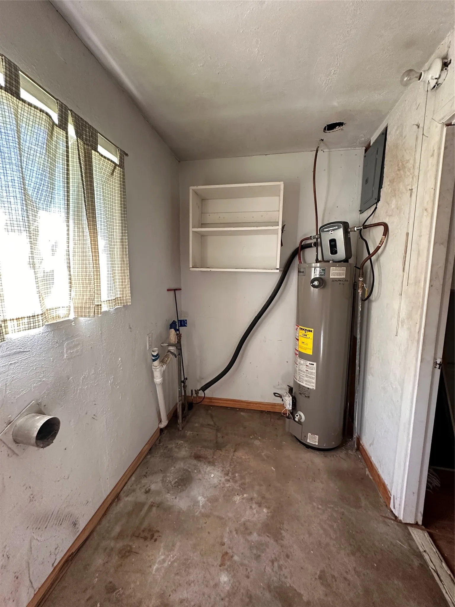 Wall-mounted shelving unit with concrete flooring and a hot water heater, washer and dryer hookups