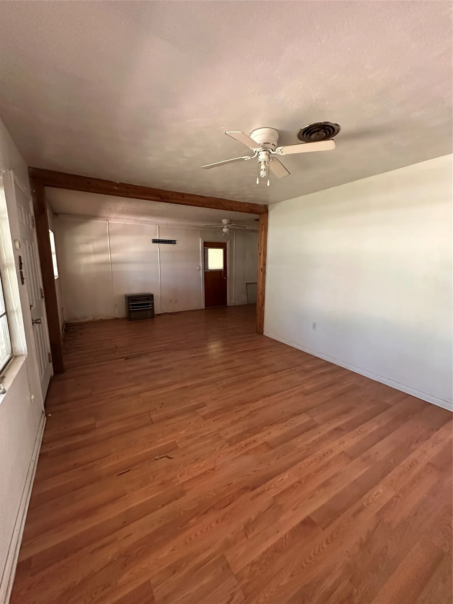 Expansive room featuring wood-finish flooring, exposed wood beam, and two ceiling fans
