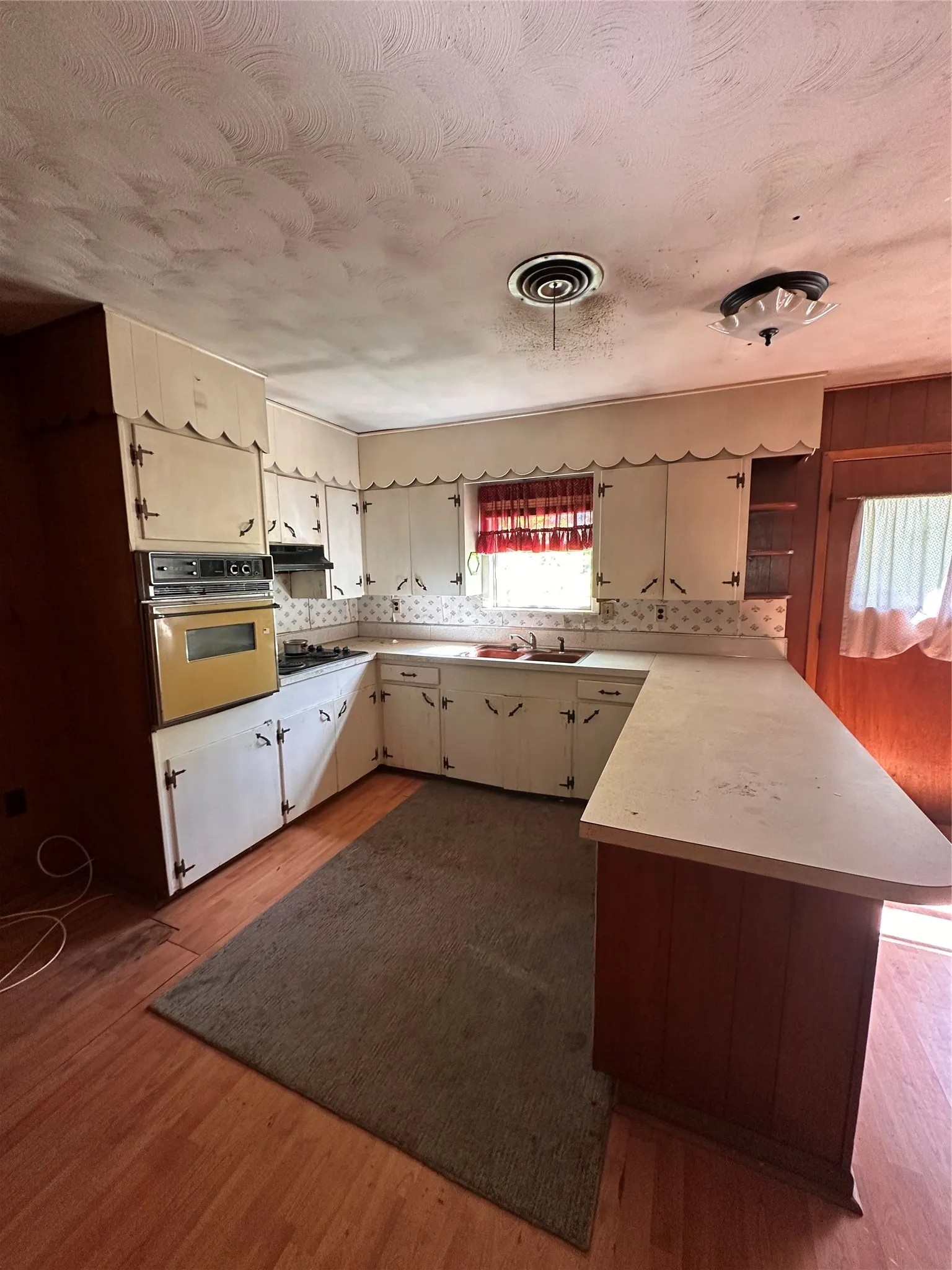 U-shaped kitchen layout with wood-finish flooring, white cabinetry, a built-in oven, and a gas cooktop