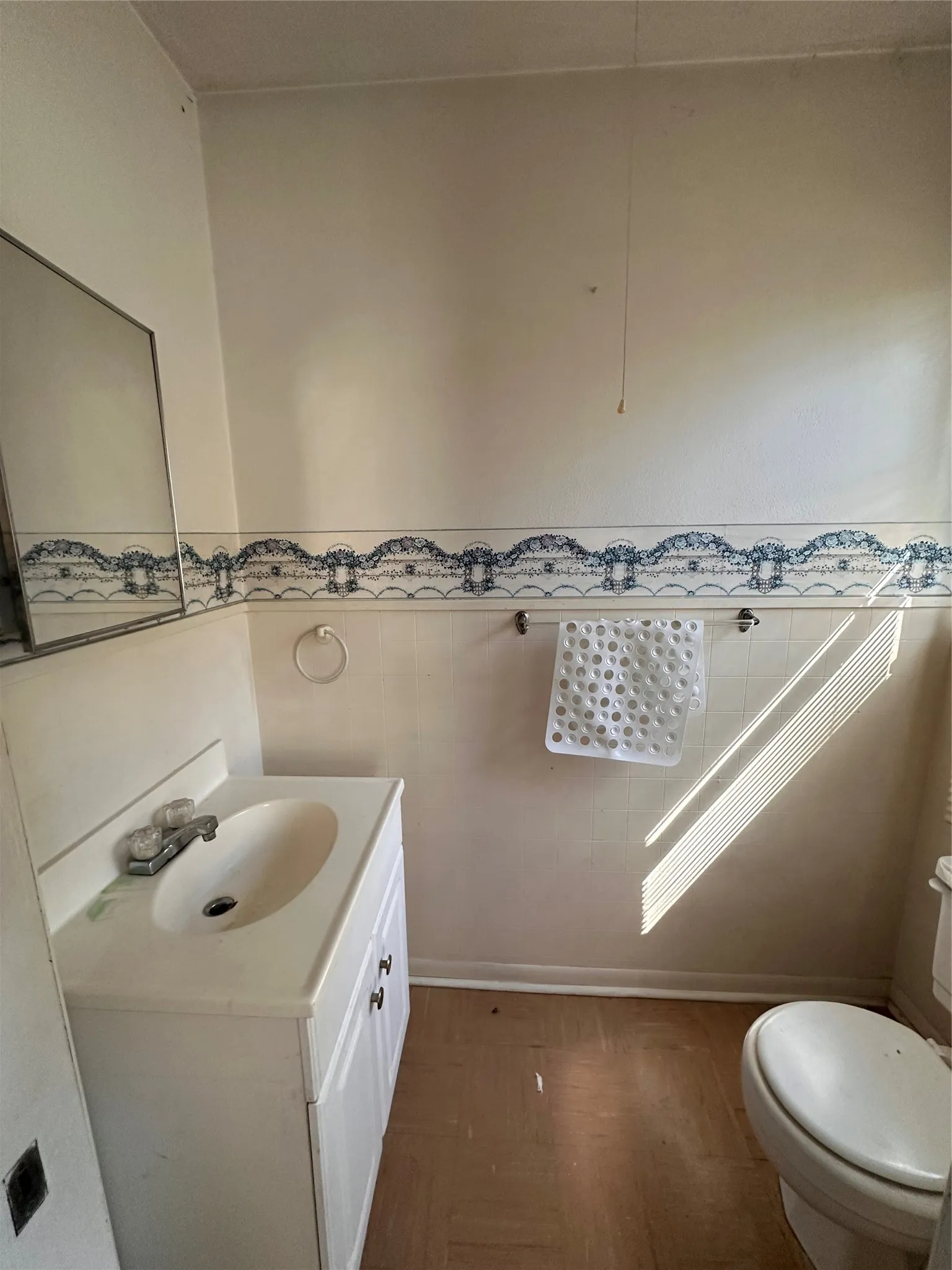 Half Bath - White vanity with integrated sink, chrome faucet, wall-mounted mirror, and tile wainscoting, toilet