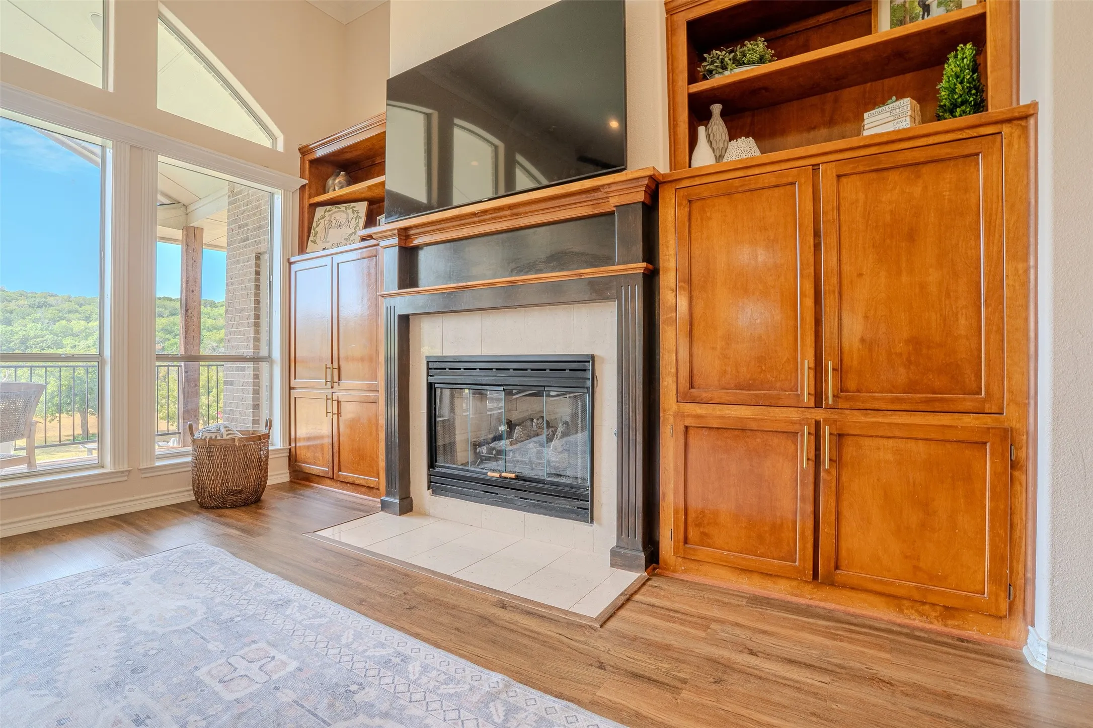 Built-in cabinetry with open shelving, wood-finish flooring, fireplace with tile surround, and large windows with transom architectural details