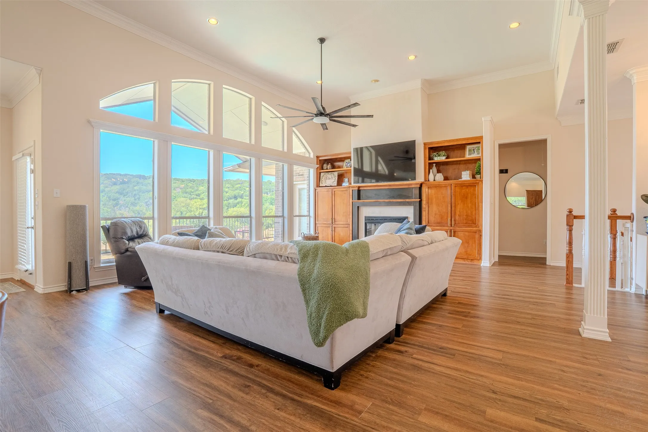 Spacious living area featuring expansive arched windows, wood-finish flooring, built-in cabinetry, and a ceiling fan