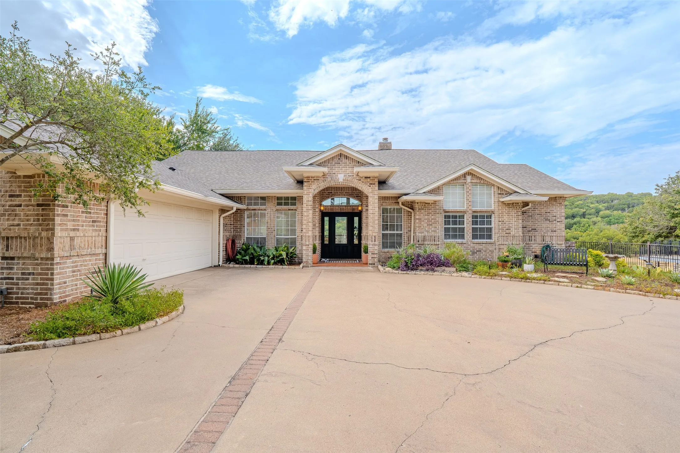 Brick-clad exterior with a prominent arched entry, multi-pane windows, an attached two-car garage, and a concrete driveway with brick accents