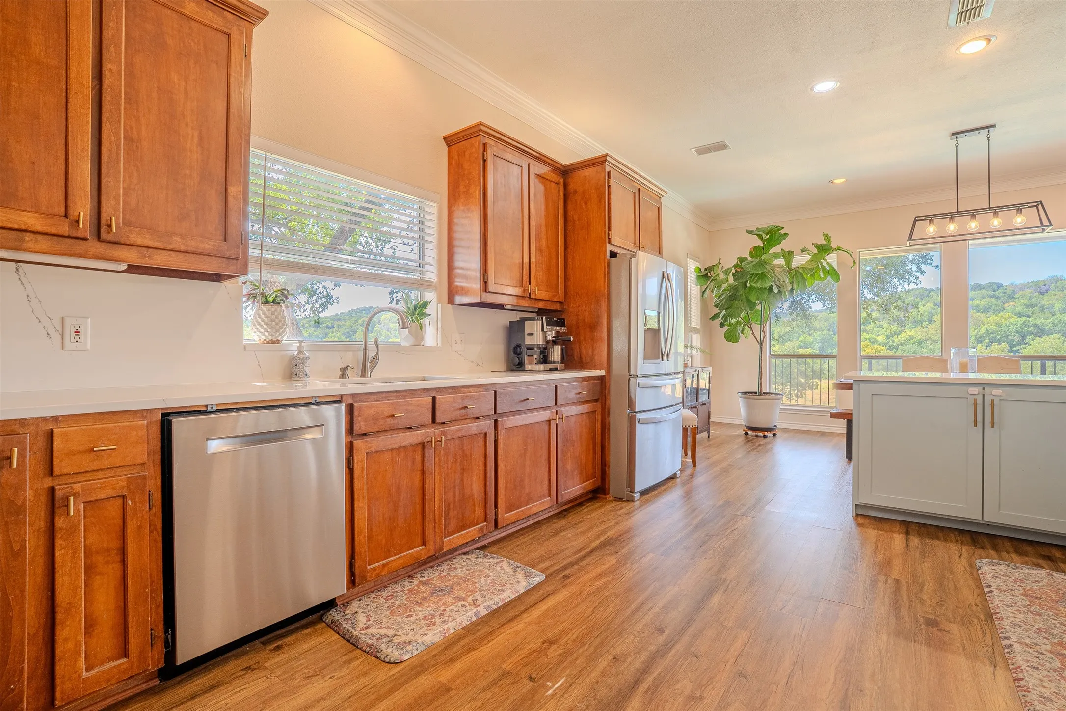 Kitchen featuring wood-finish flooring, stainless steel appliances, wood cabinetry, light-toned countertops, and an island with pendant lighting