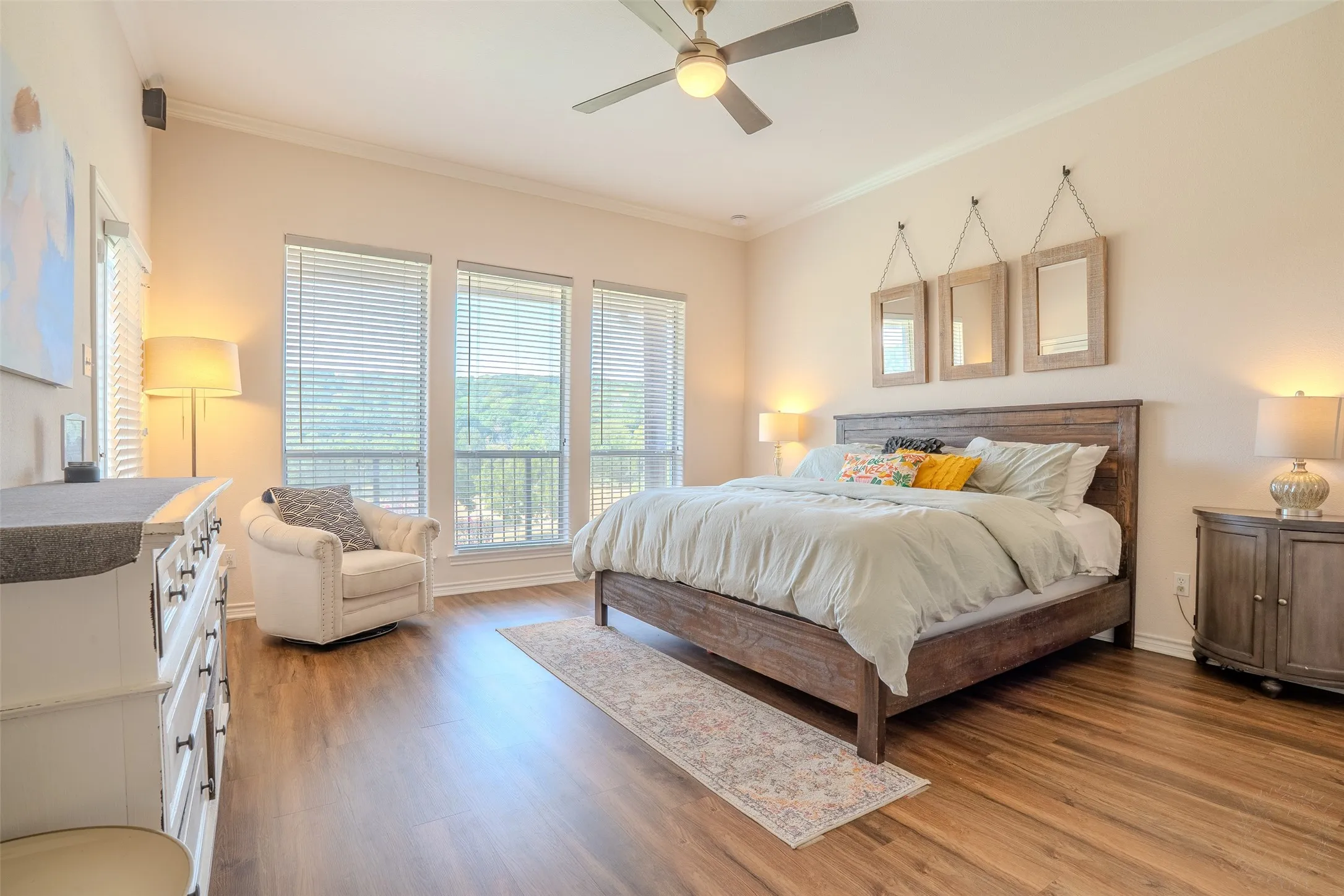 Wood-finish flooring, crown molding, ceiling fan with integrated lighting, and multiple windows with horizontal blinds