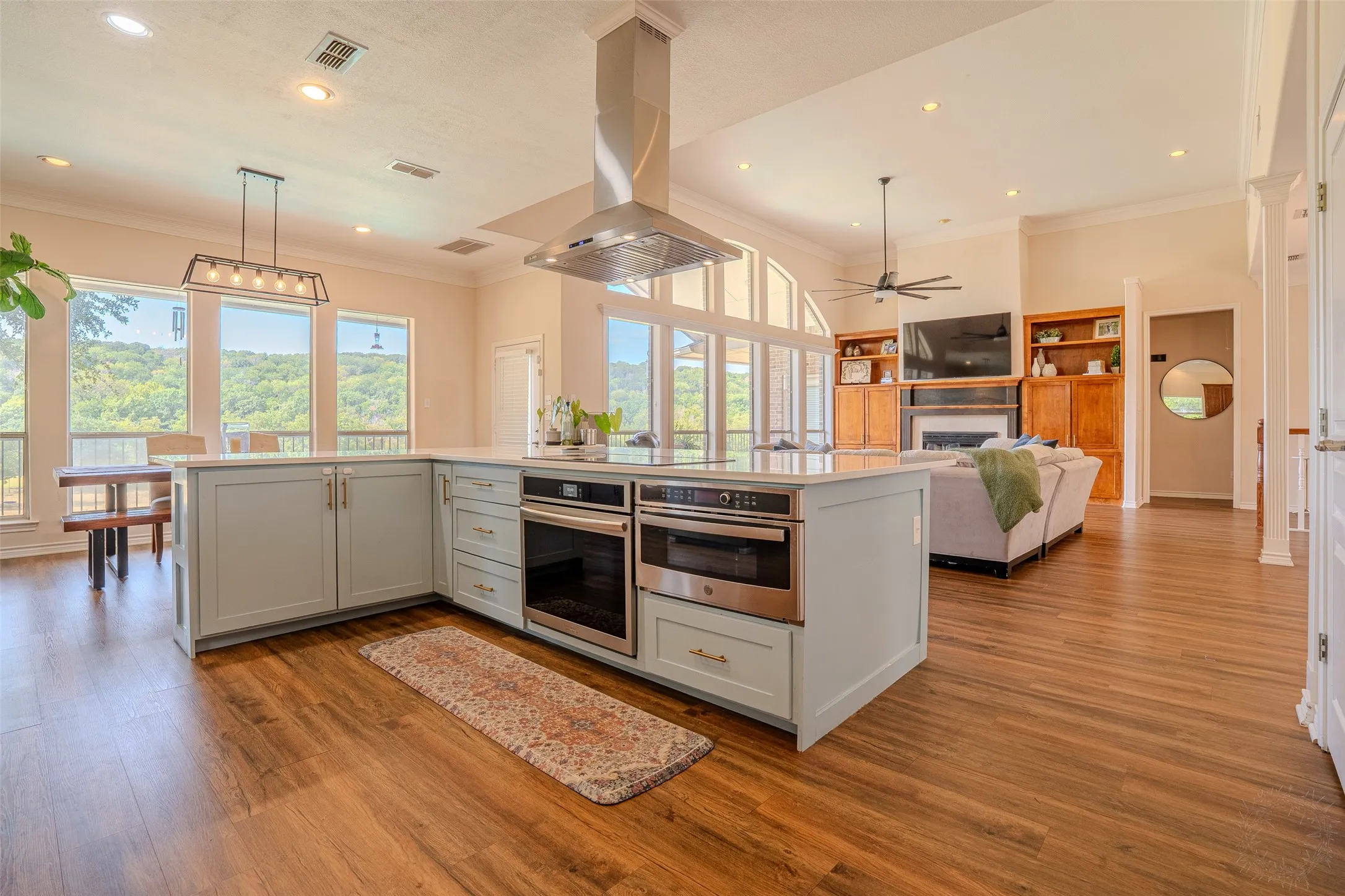 Spacious open-concept interior featuring wood-finish flooring, a kitchen island with built-in appliances, and recessed lighting