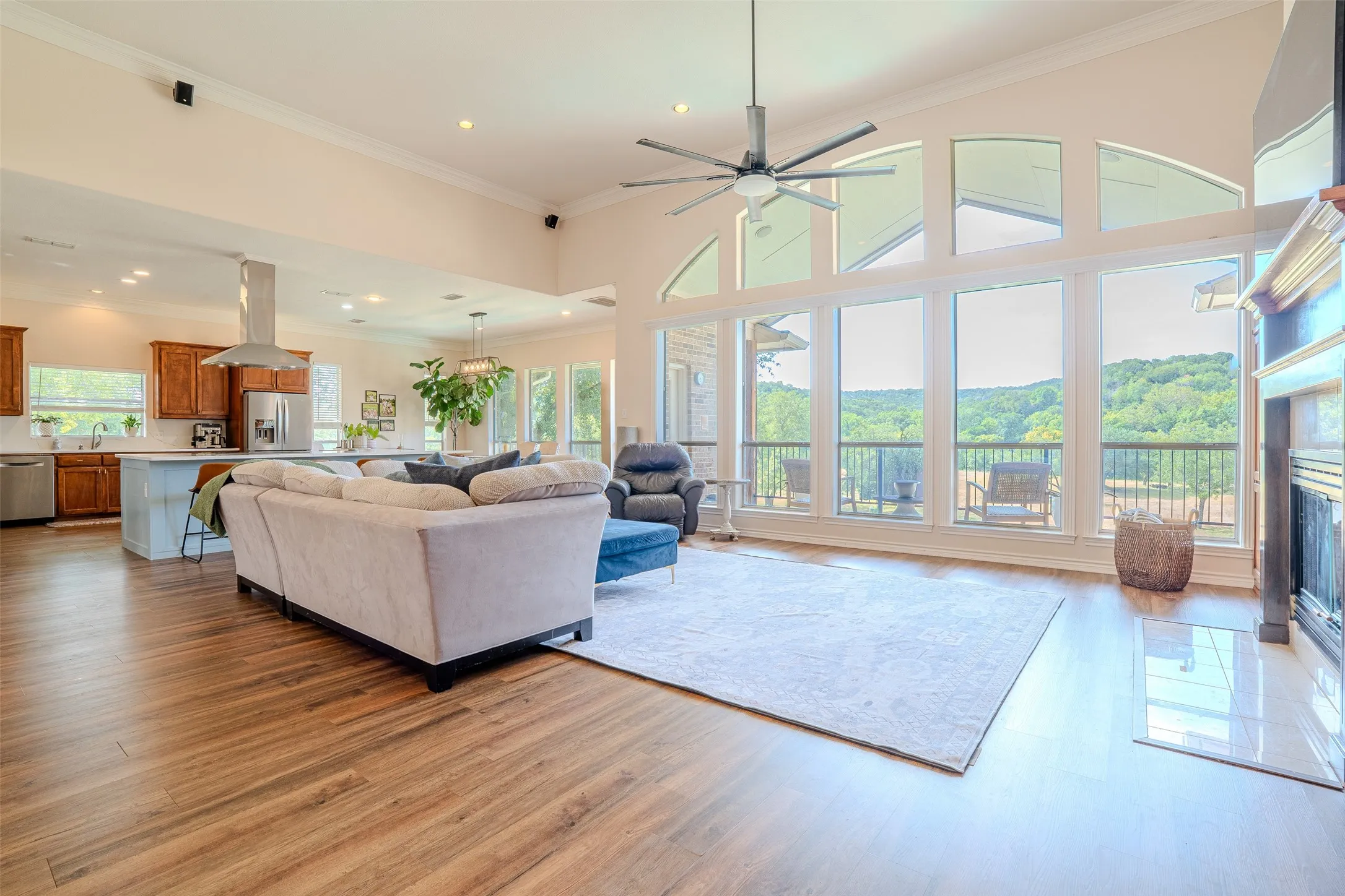 Open-concept living space with vaulted ceilings, expansive windows, wood-finish flooring, a built-in fireplace, and a kitchen island with seating