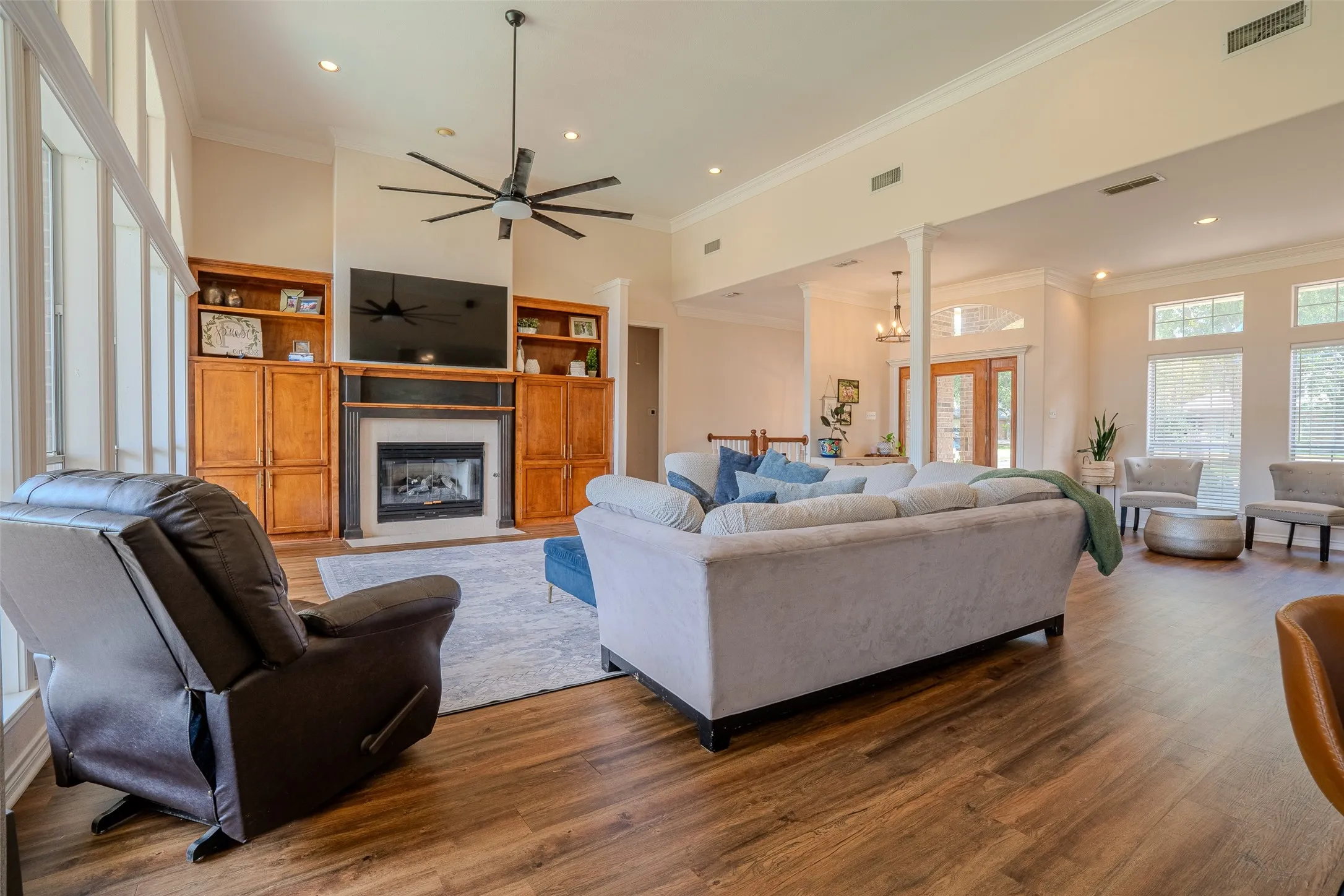 Wood-finish flooring throughout, featuring a fireplace with built-in cabinetry, an angular ceiling, recessed lighting, and a prominent ceiling fan
