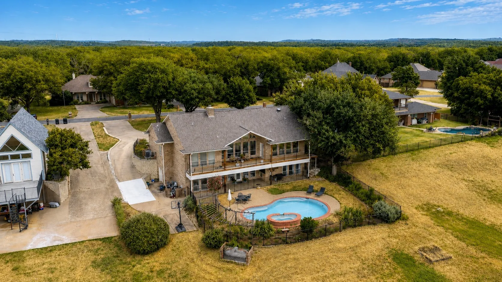 Stone exterior with multiple balconies, a fenced swimming pool with an integrated spa, and an expansive paved driveway