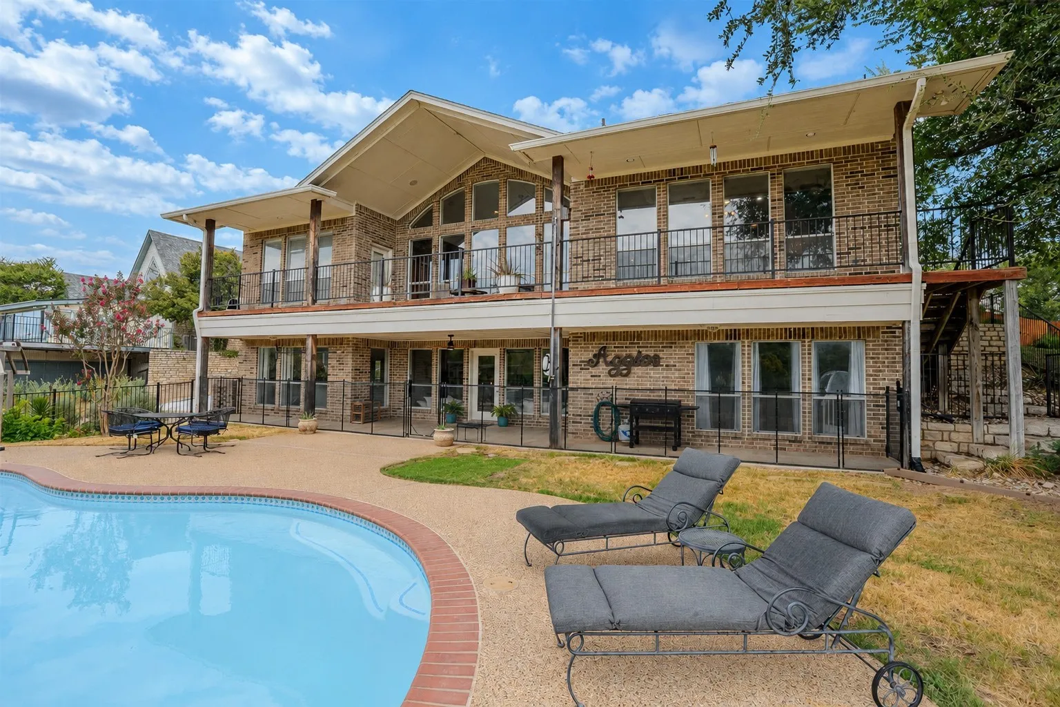 Brick exterior with multiple balconies, a large swimming pool, and a spacious paved patio