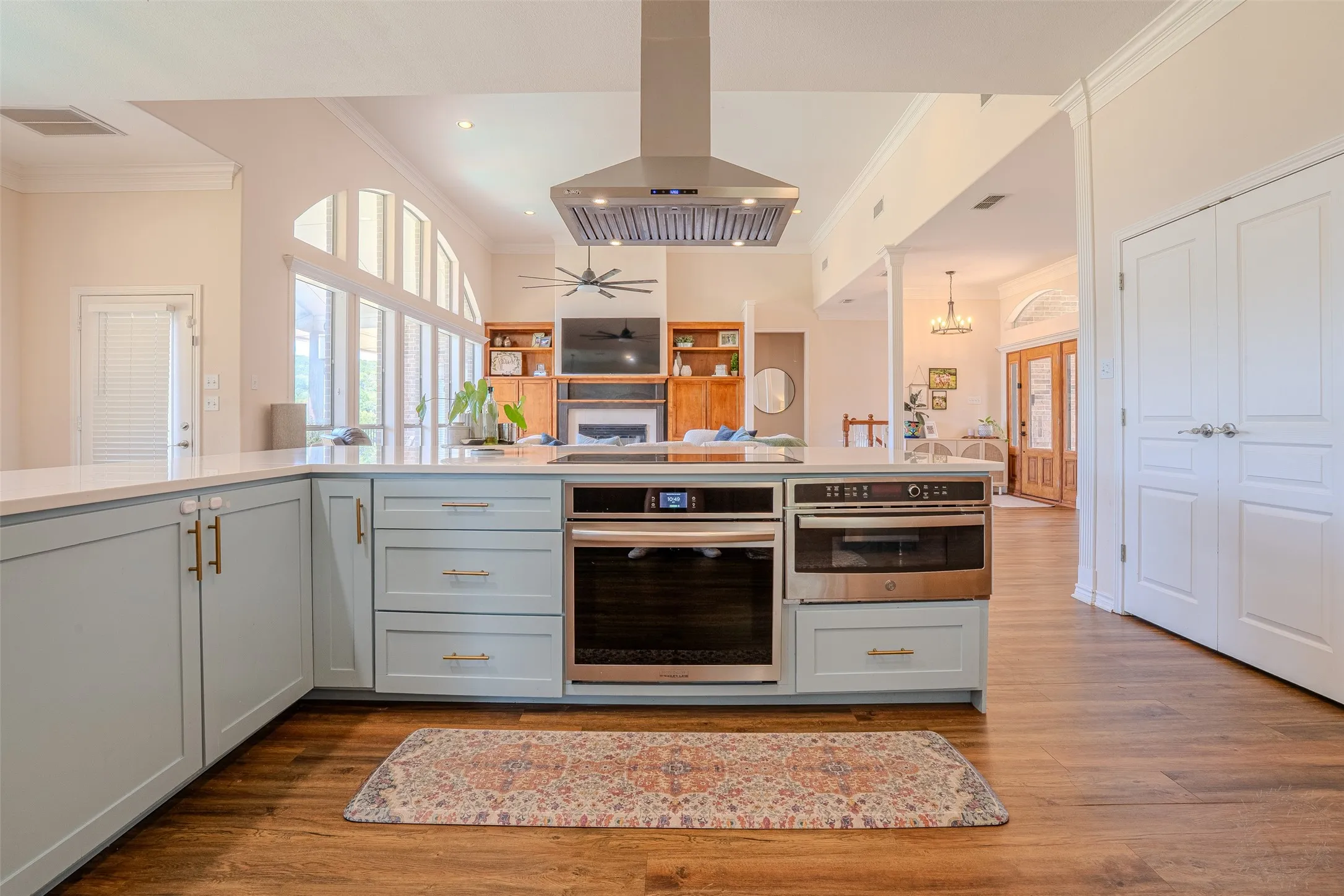 Kitchen island with light blue cabinetry, built-in stainless steel oven, and integrated microwave, complemented by wood-finish flooring and a stainless steel range​​‌​​​​‌​​‌‌​‌‌​​​‌‌​‌​‌​‌​​​‌​​ hood
