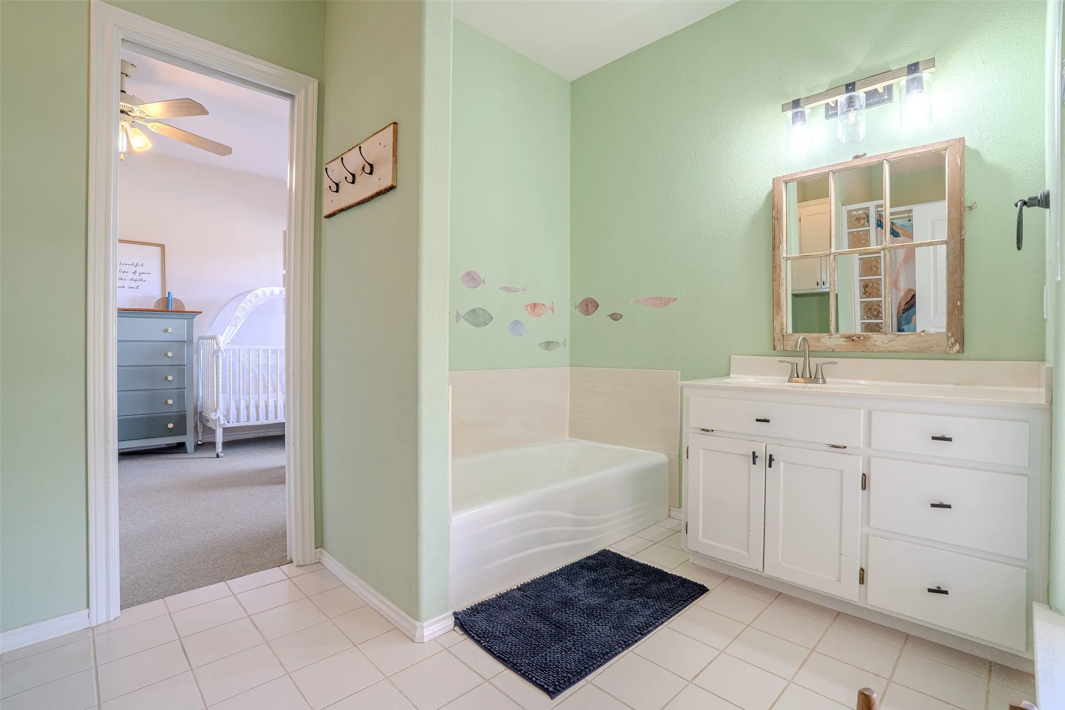 White tile flooring, built-in bathtub, white vanity with integrated sink, and wall-mounted light fixture