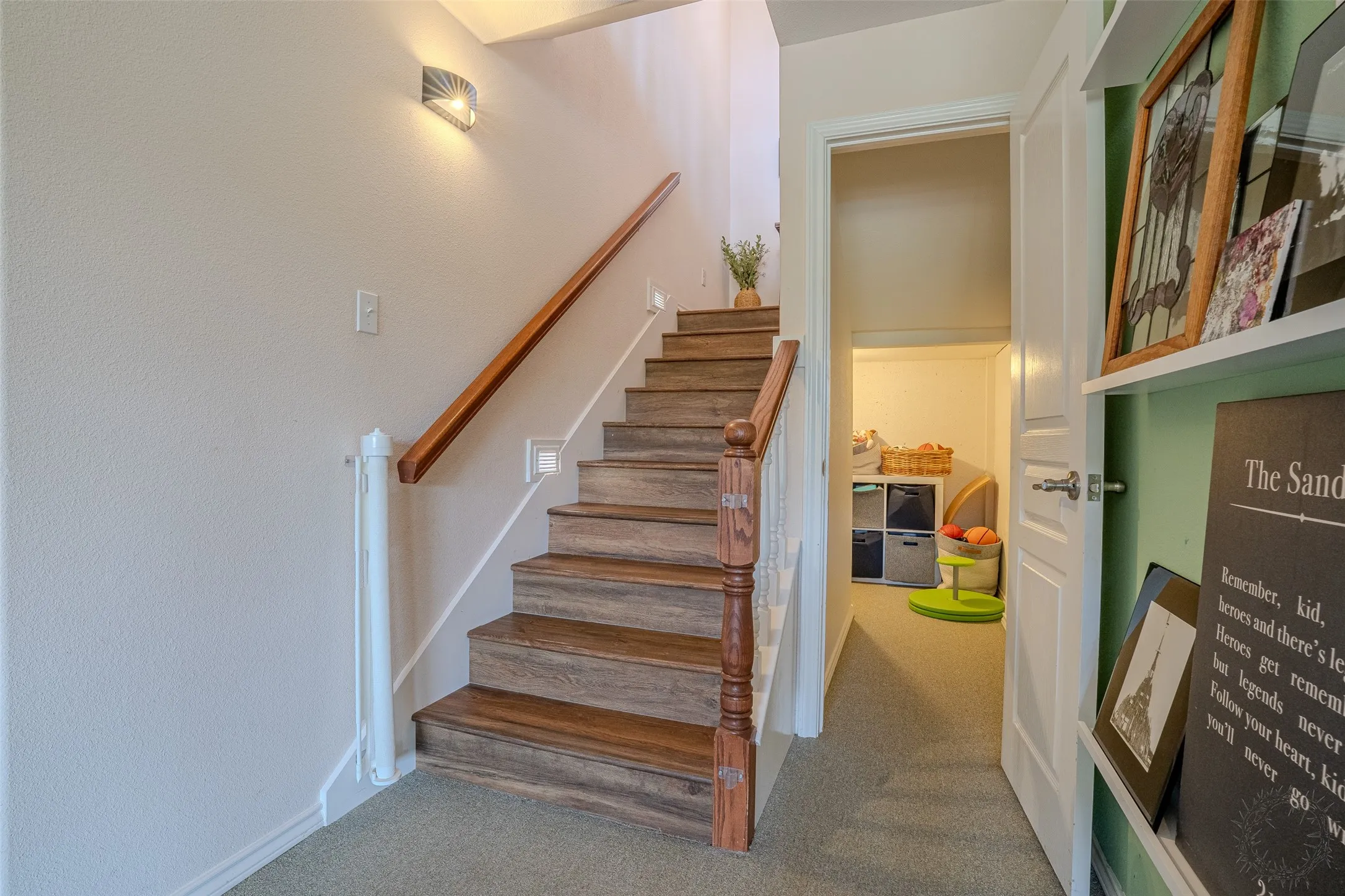 Hardwood-finish stairs with a wood handrail, wall-mounted lighting, and carpeted floor