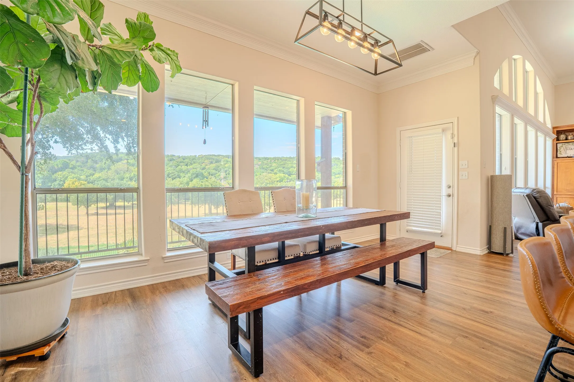 Expansive windows offering natural scenery, wood-finish flooring, a built-in arched window feature, and a modern rectangular chandelier
