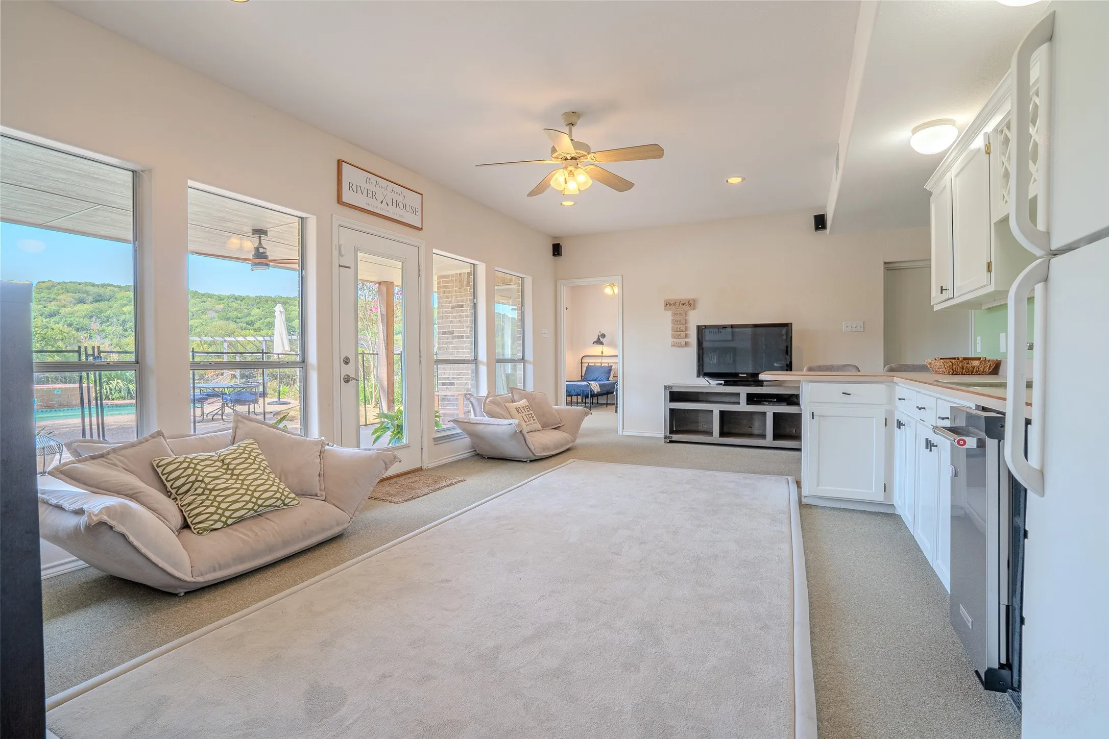 Spacious living area with multiple large windows, glass-paneled door, ceiling fan, and recessed lighting