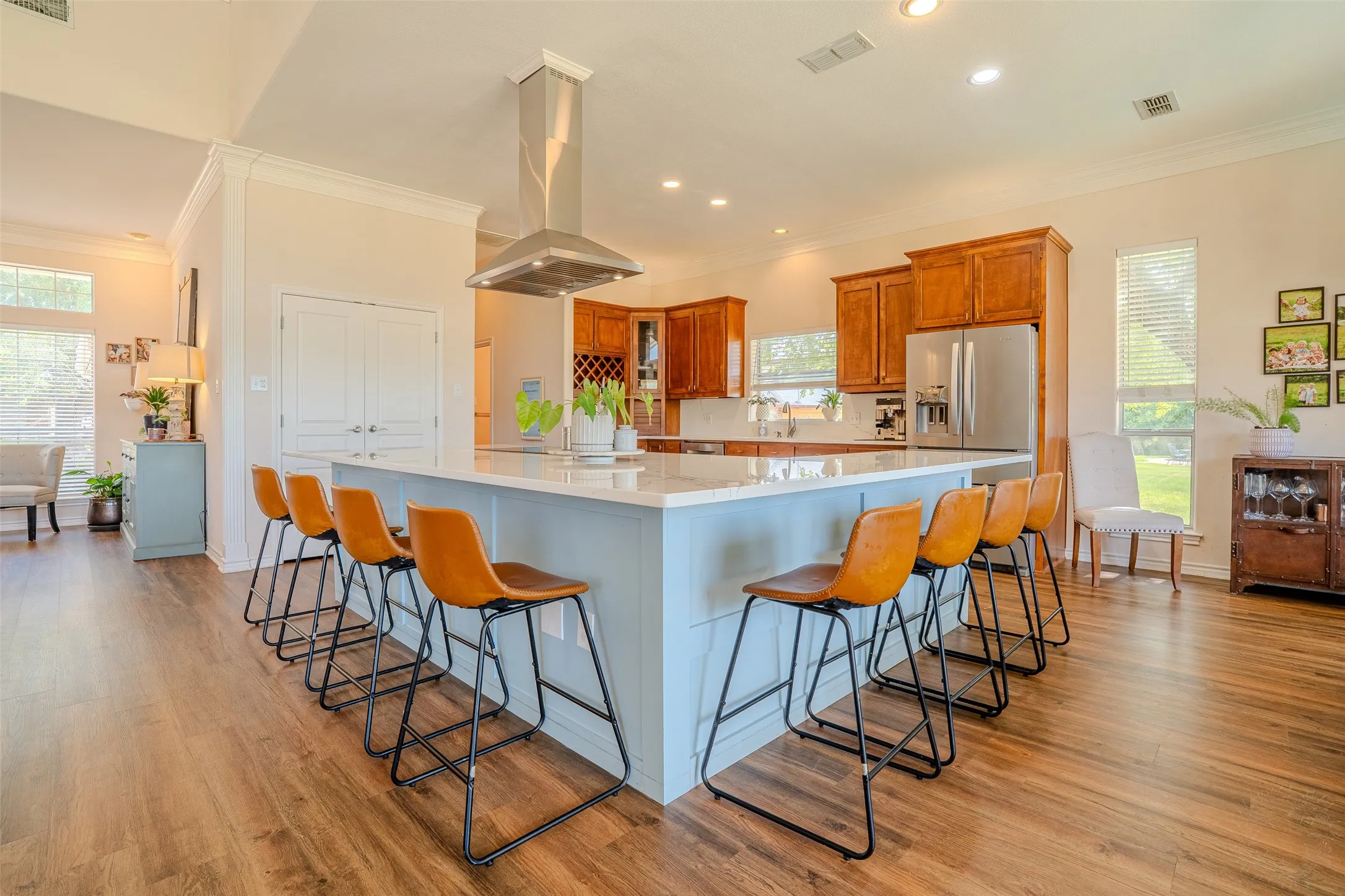 Open-concept kitchen with wood-finish flooring, a light blue island with a stone countertop, stainless steel appliances, and wood cabinetry