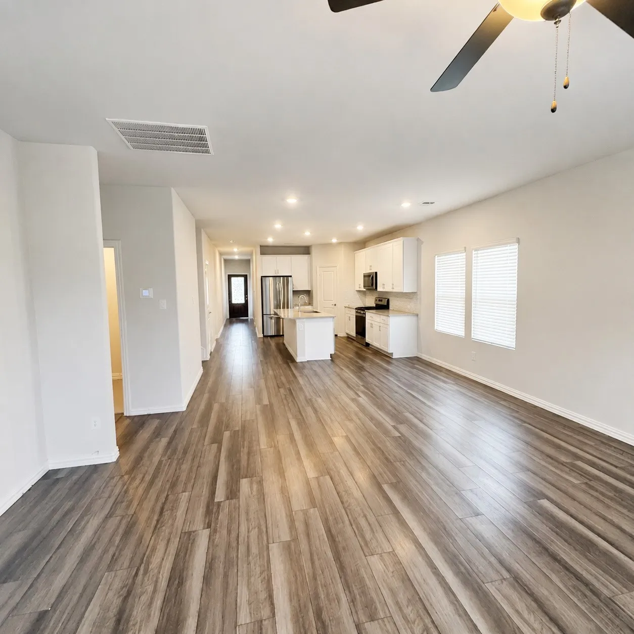 Wood-finish flooring throughout, recessed lighting, ceiling fan, white kitchen cabinetry, and stainless-steel appliances