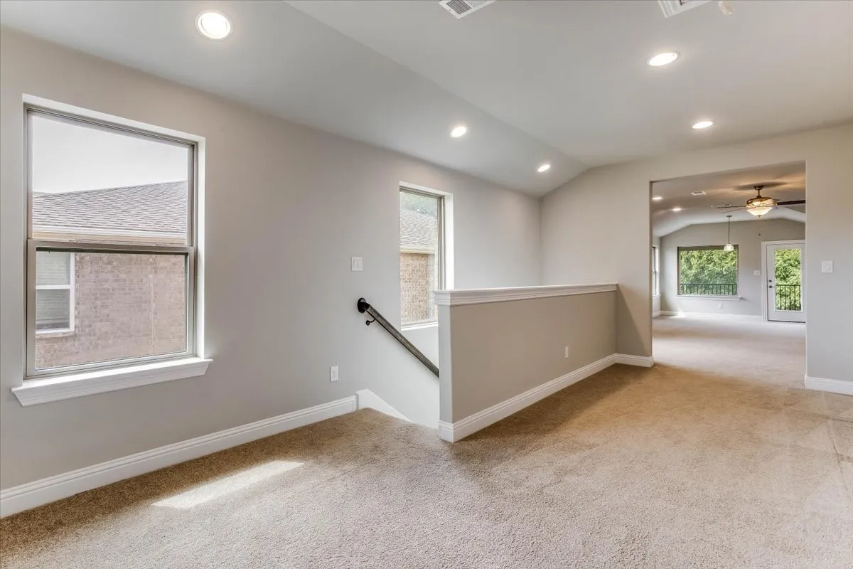 Bright second-floor loft with neutral carpeting, half-wall banister overlooking the stairwell, recessed lighting, and seamless flow into adjacent living areas. This could be a library, study area, the ideas of endless.