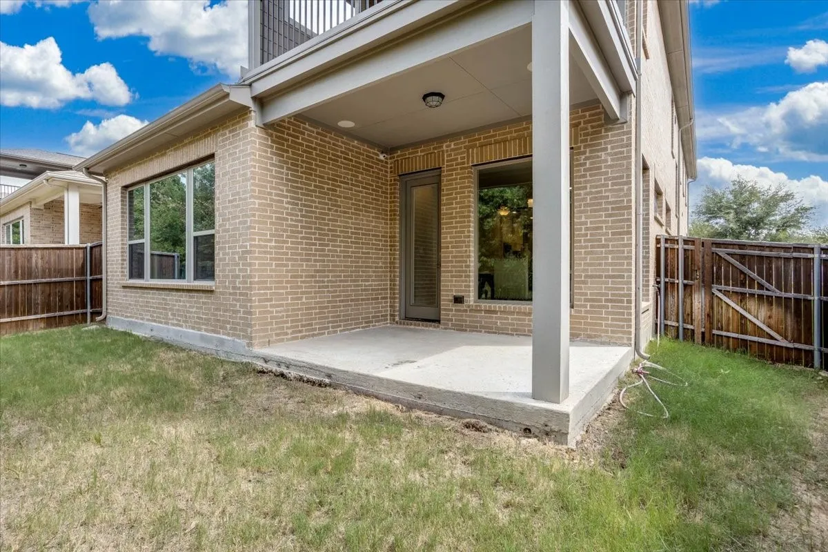 Covered brick patio with concrete pad, perfect for outdoor dining, nestled directly beneath a private second-story balcony. Covered back patio nestled beneath a private balcony—an ideal spot for outdoor relaxation overlooking mature trees and a quiet greenbelt.
