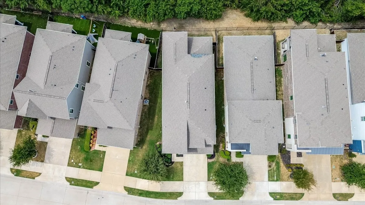 Aerial bird's-eye photo showcasing the home's roofline, private lot layout, paved driveway, and immediate proximity to the lush rear greenbelt