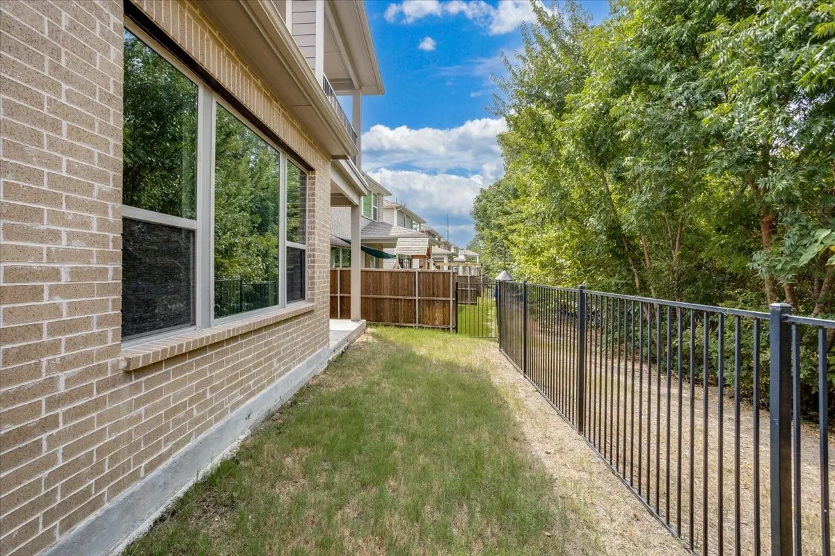 Low-maintenance side yard featuring clean wrought-iron fencing that offers clear views of the serene, tree-lined greenbelt behind the home.