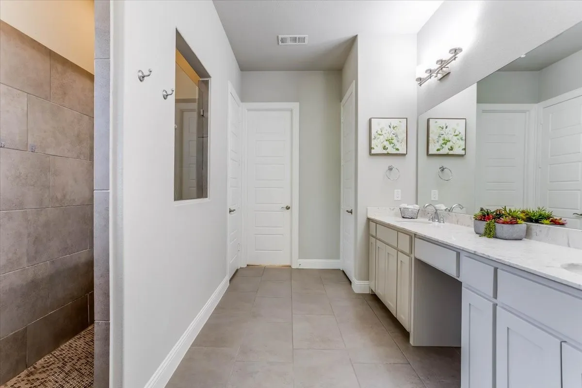 Spa-like primary bath boasting a double vanity with ample counter space, a dedicated makeup station, tiled flooring, and a large walk-in glass shower enclosure.