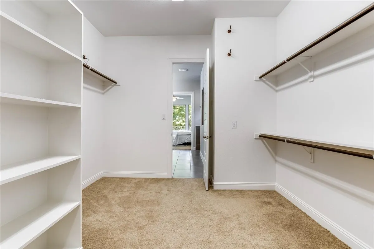 Generous walk-in closet off the primary bath featuring built-in shelving towers, multi-tier hanging rods, and plush neutral carpeting.