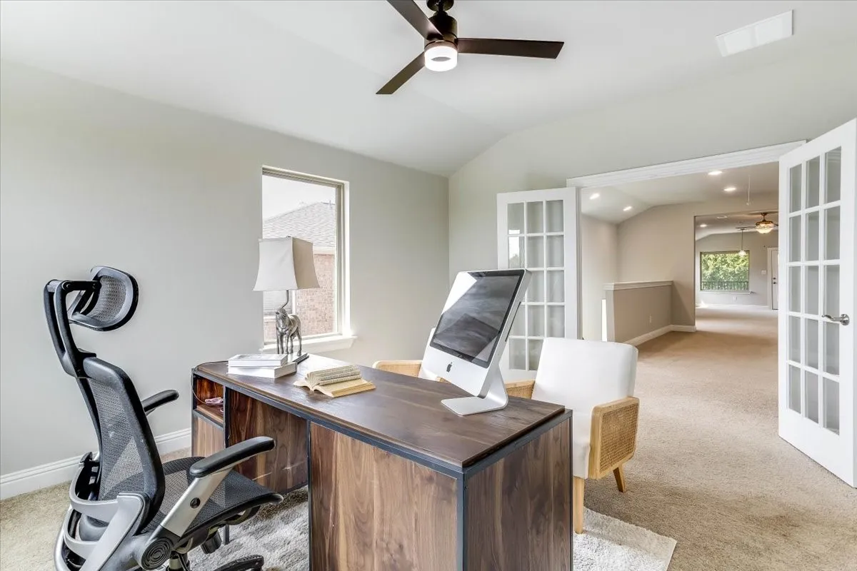 Private home office featuring double French doors, bright window natural light, plush carpet, and a modern ceiling fan
